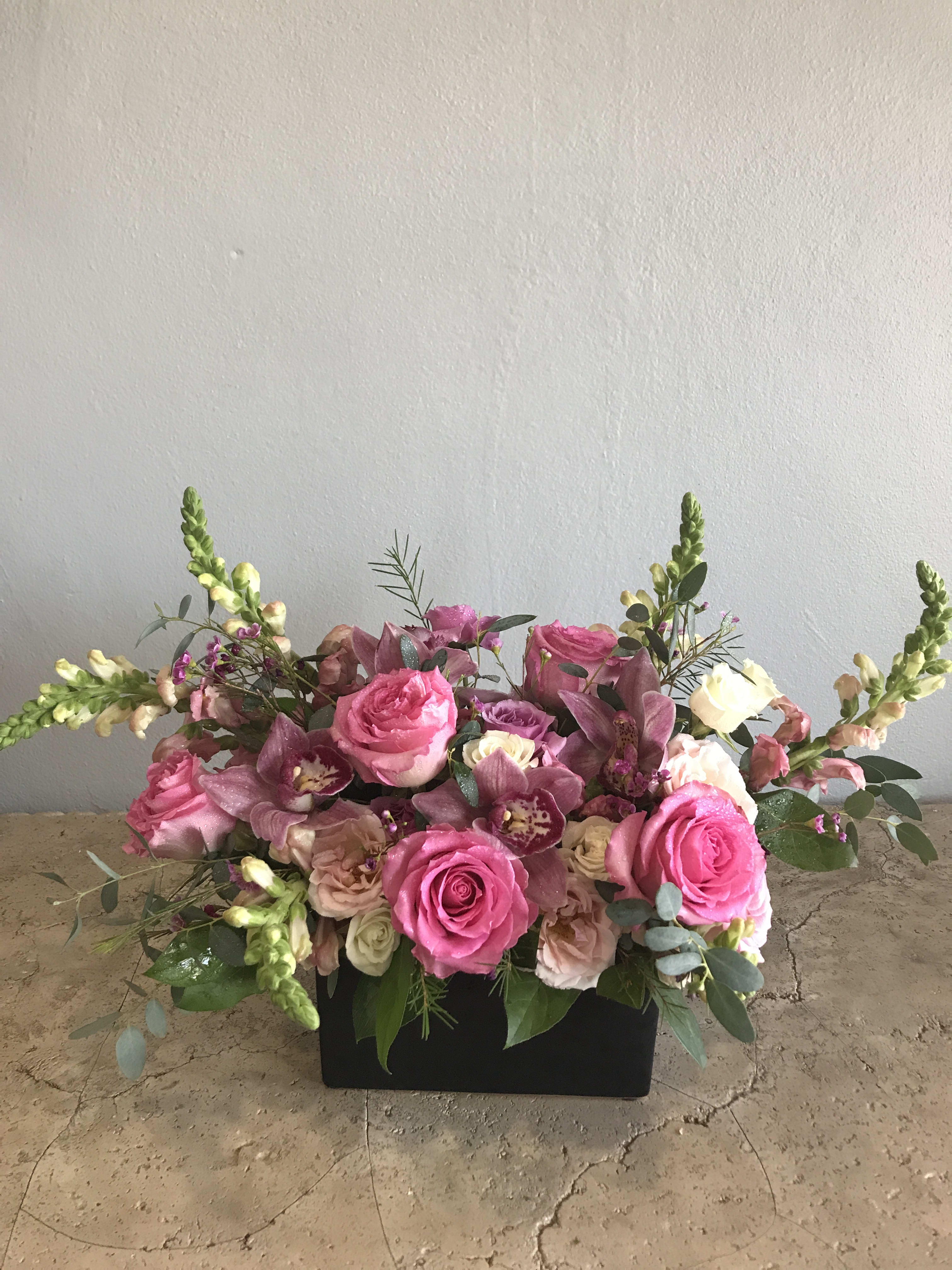 Pink roses and purple orchids in a black rectangular container