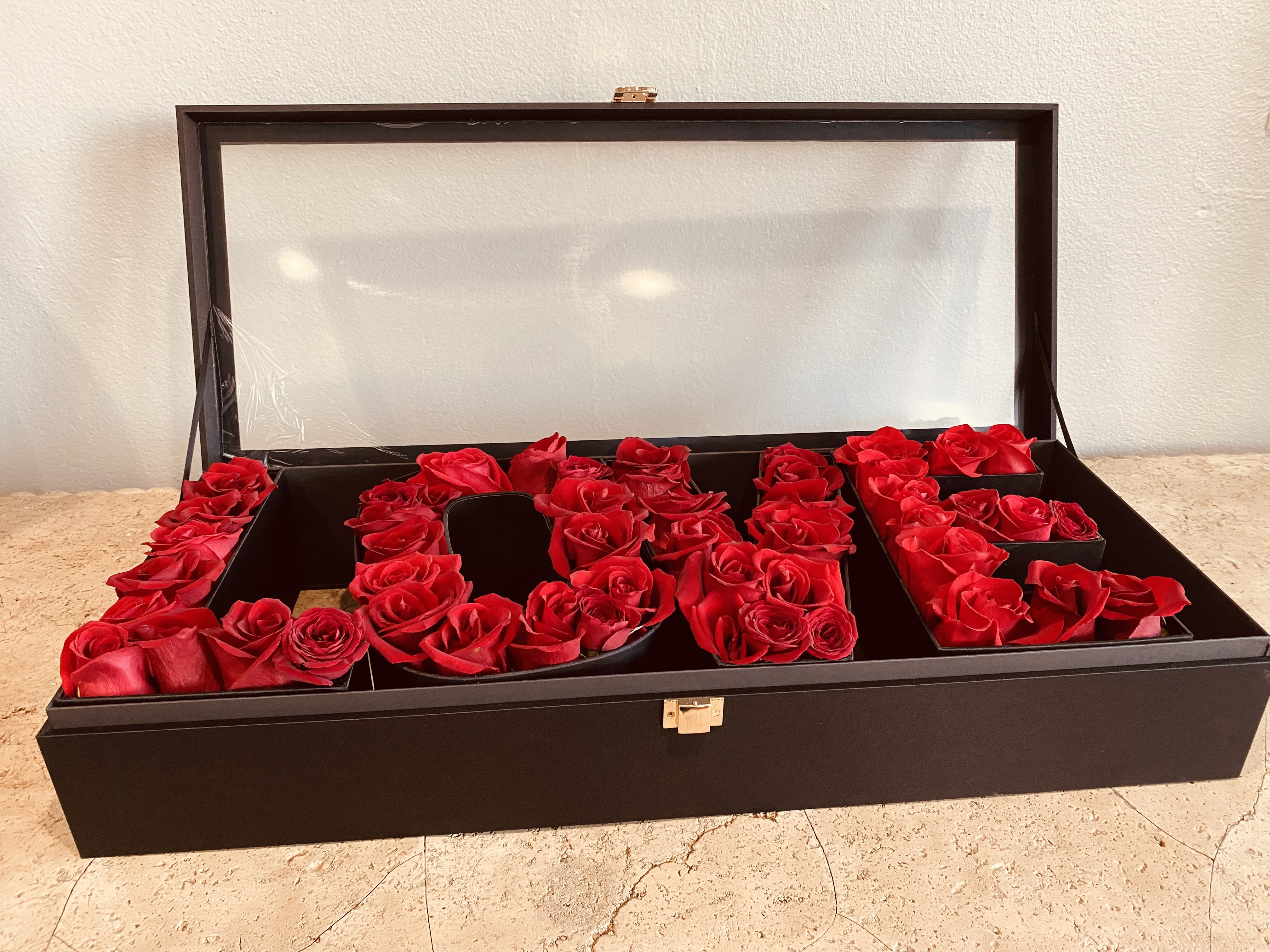 Red roses arranged in a black display box with a clear lid