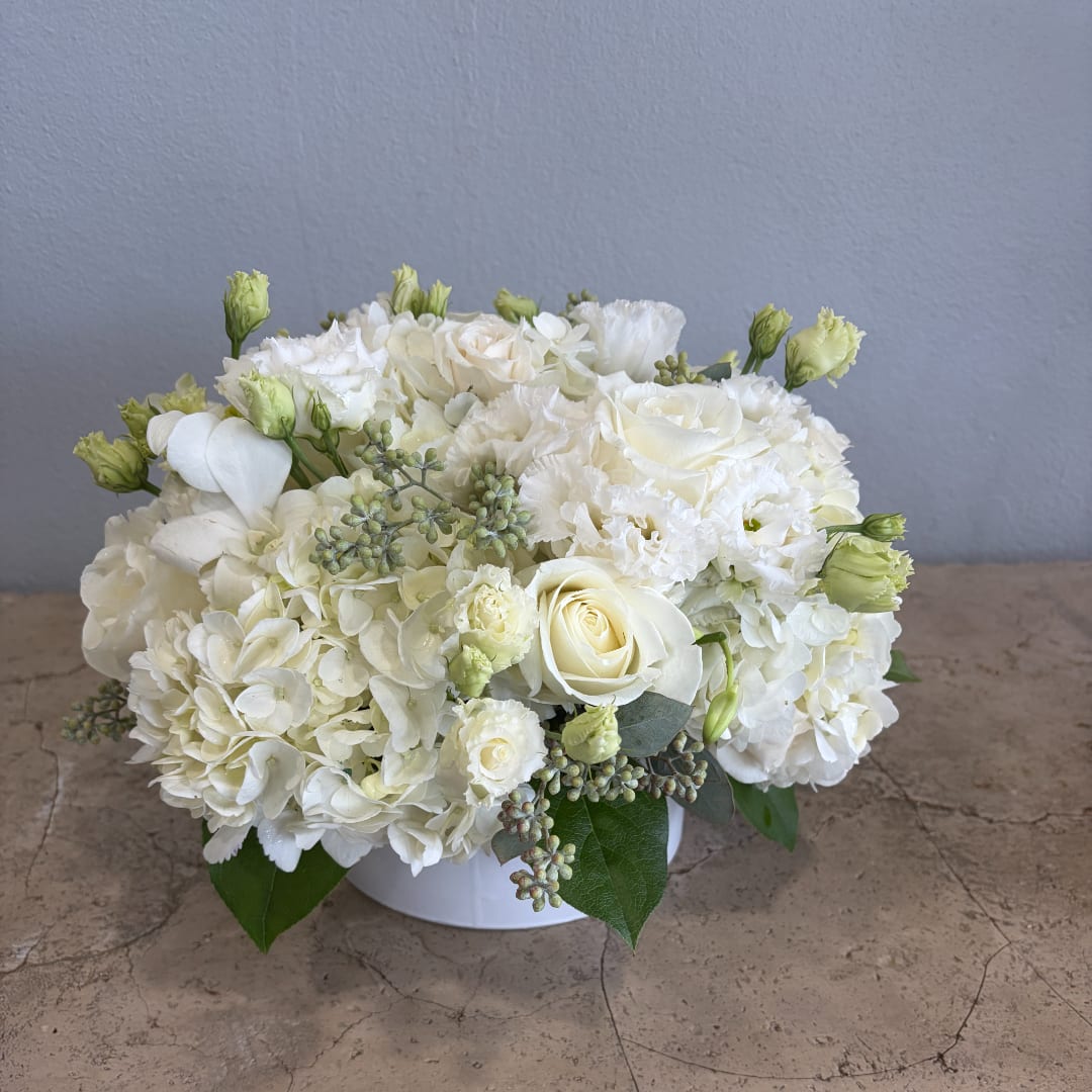 White floral arrangement in a low round vase with roses and hydrangeas