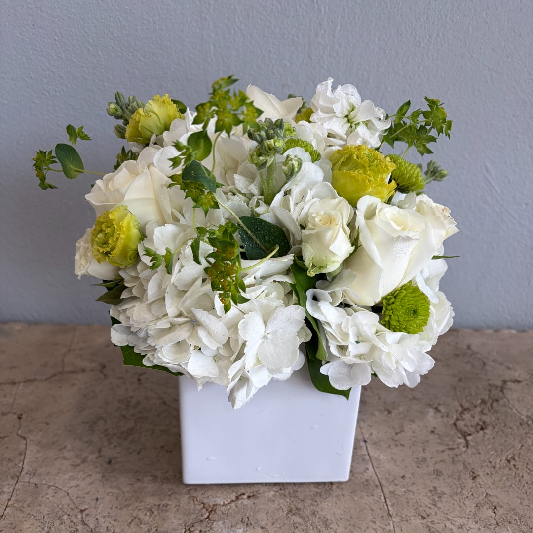 White and green floral arrangement in a square white vase