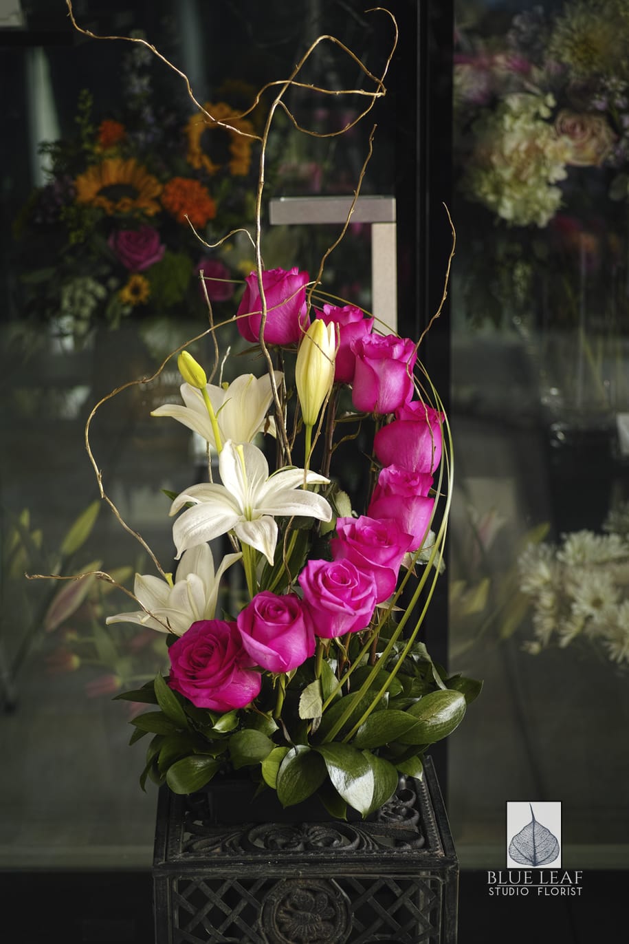 Pink roses and white lilies in a tall black container with curly branches