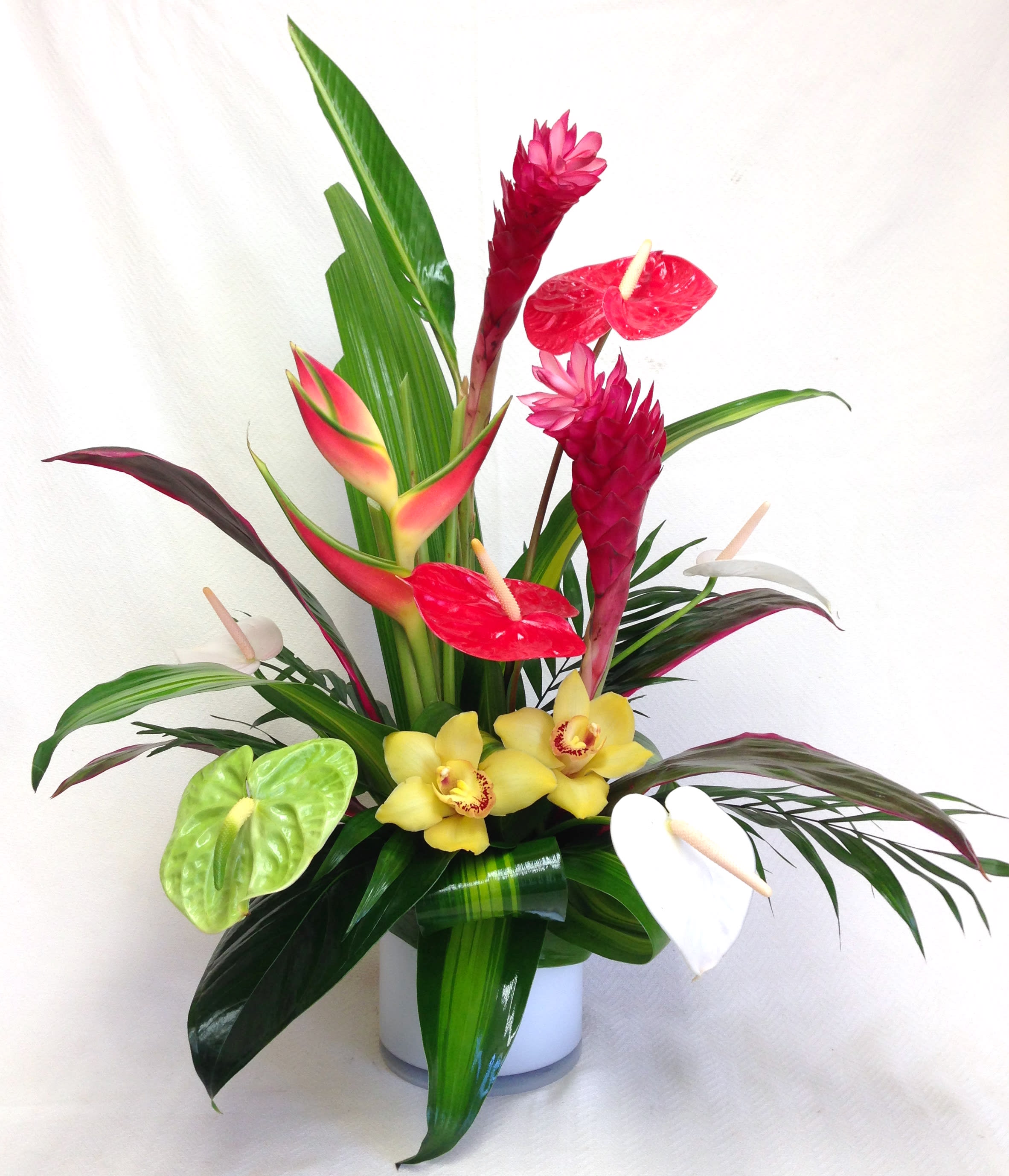 Tropical arrangement with red anthuriums and yellow orchids in a white vase