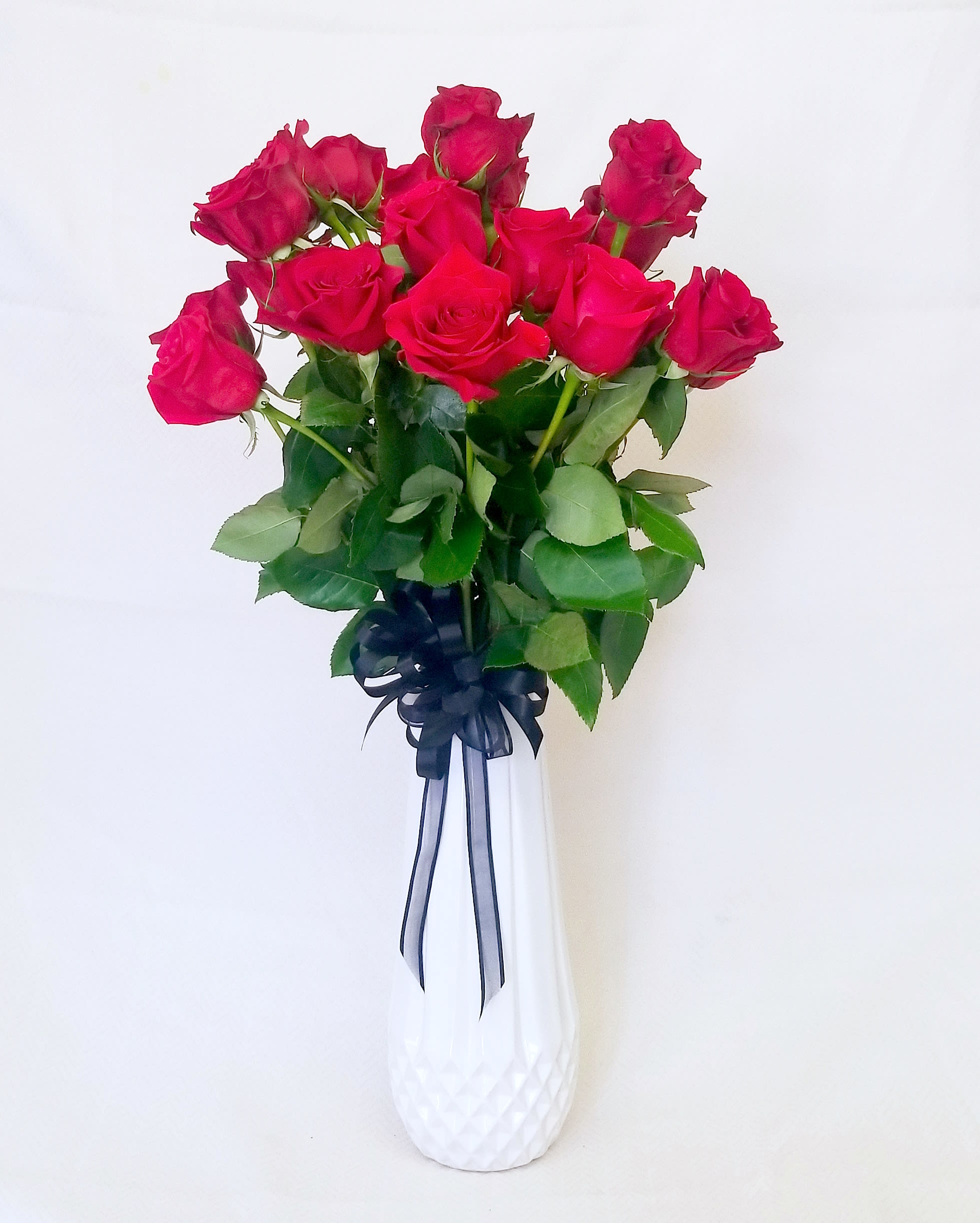 Bouquet of hot pink roses in a white vase with a dark ribbon
