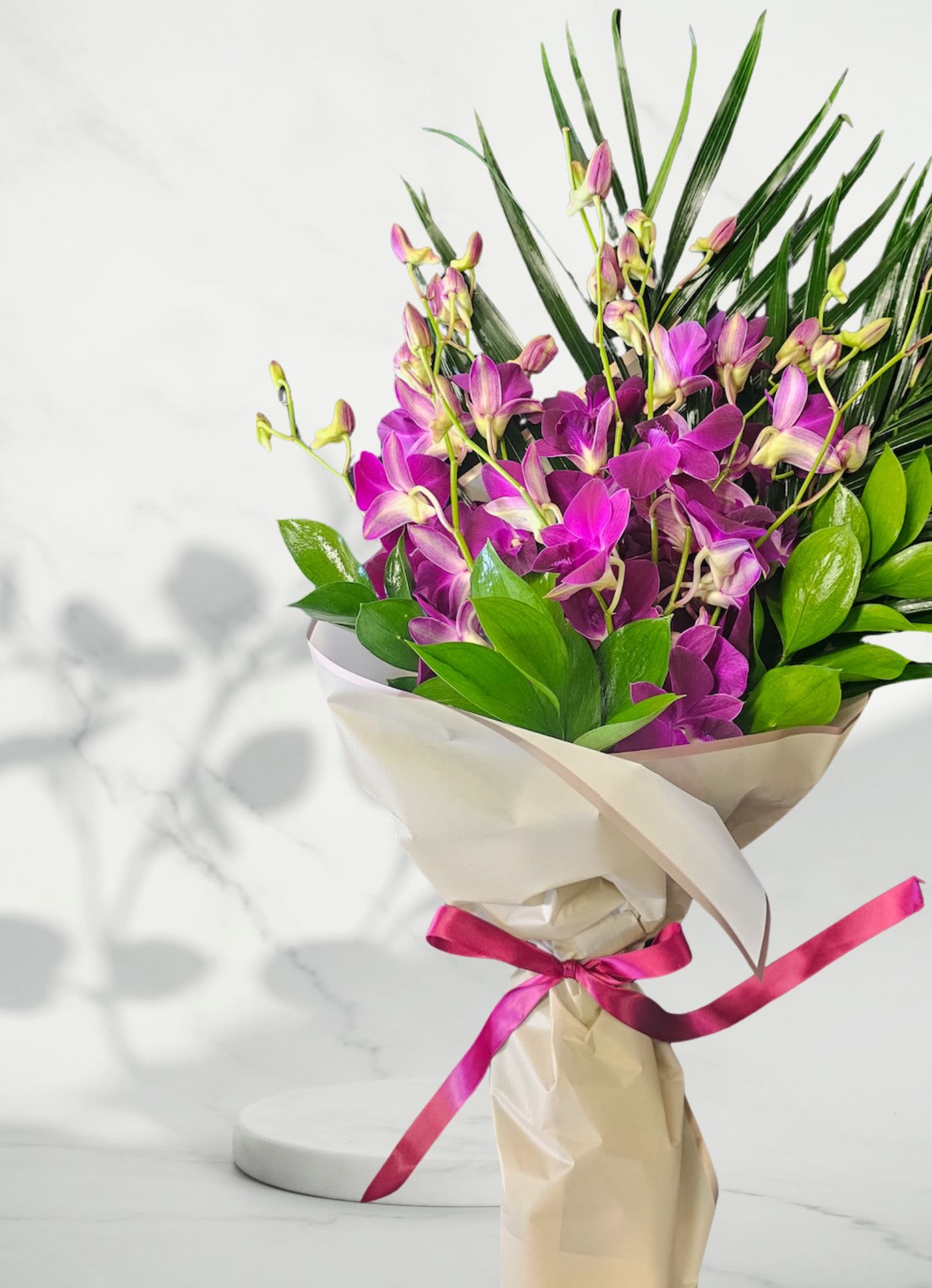 Bouquet of purple orchids wrapped in cream paper with a pink ribbon