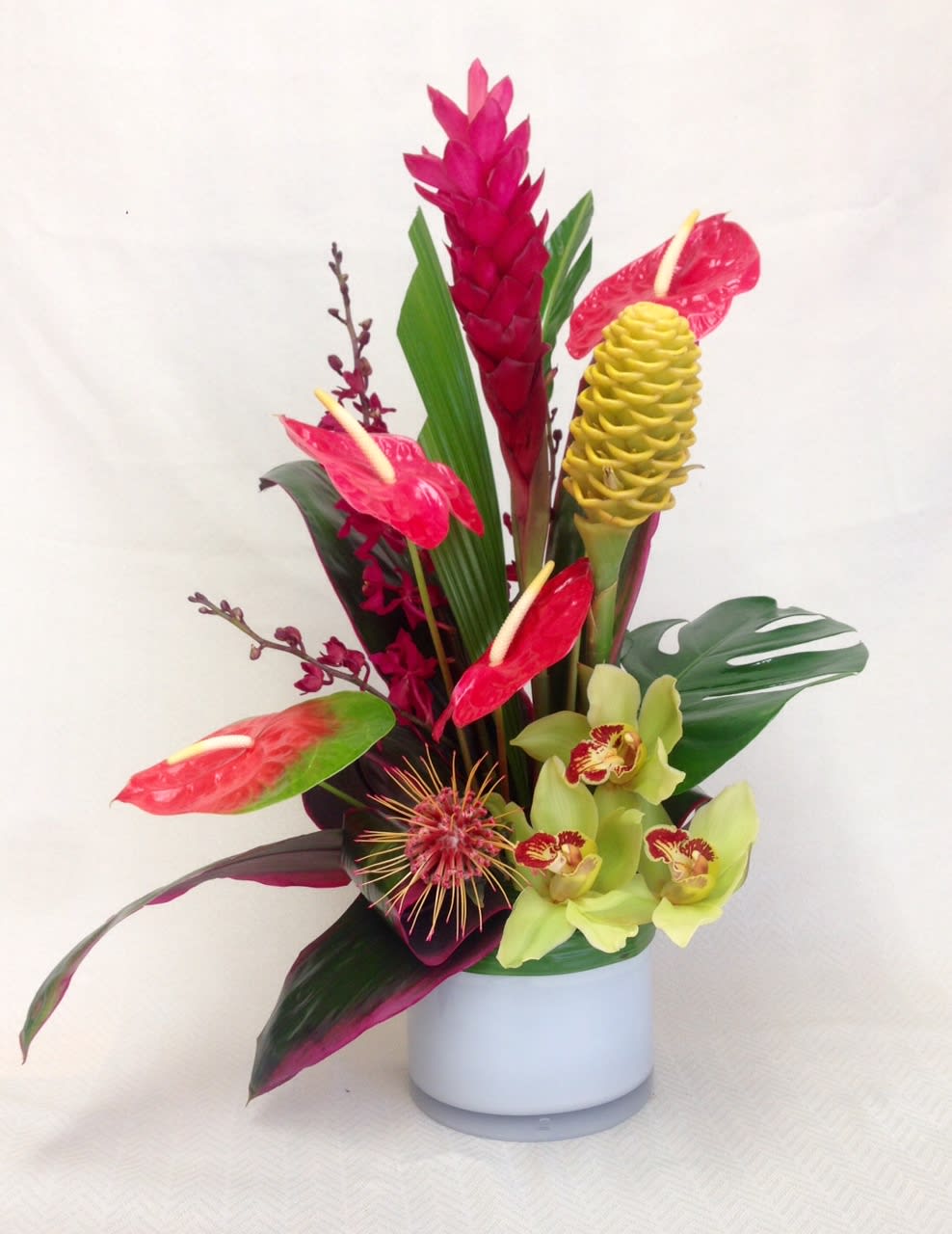 Tropical flower arrangement in a white vase with red anthuriums and yellow orchids