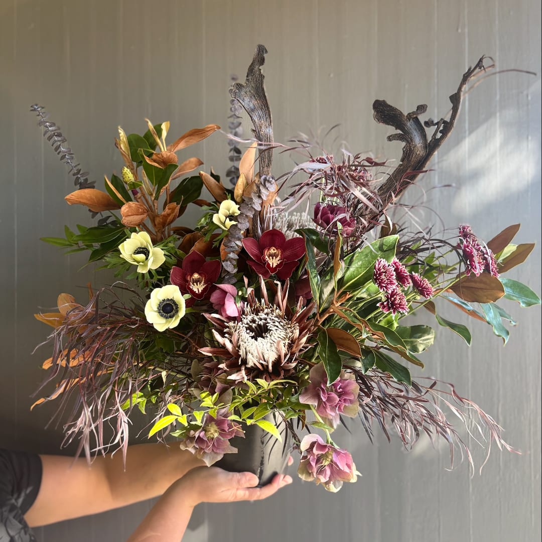 Mixed floral arrangement in a black pot with burgundy, cream, and copper blooms