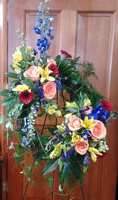 Summer Colored Standing Wreath - Grapevine wreath with fresh flowers added to it. Done in summer colors, with delphinium, gerbera daisies, roses, lilies, and other flowers with mixed greens.