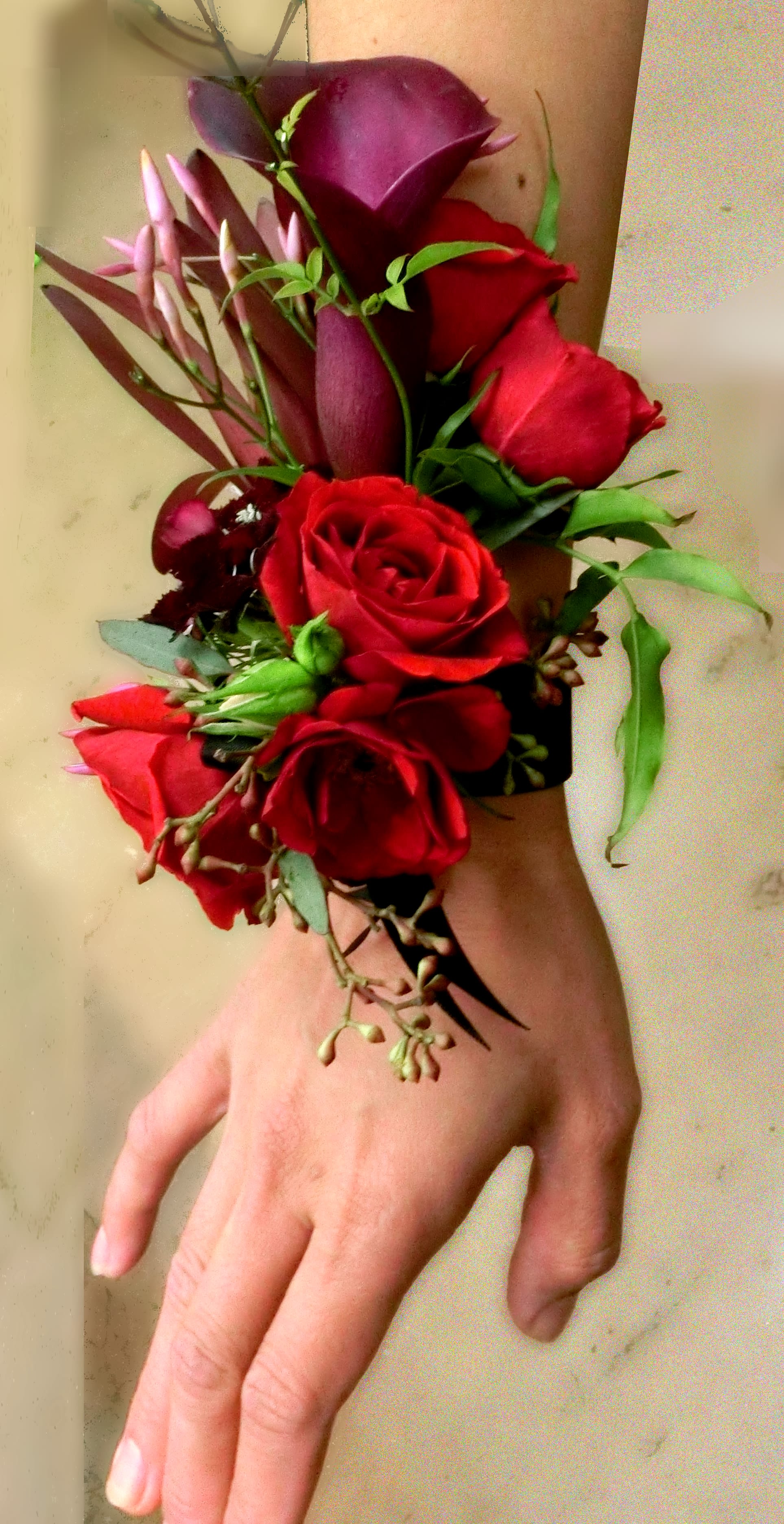 Wrist corsage with red roses and dark purple calla lilies on a black band