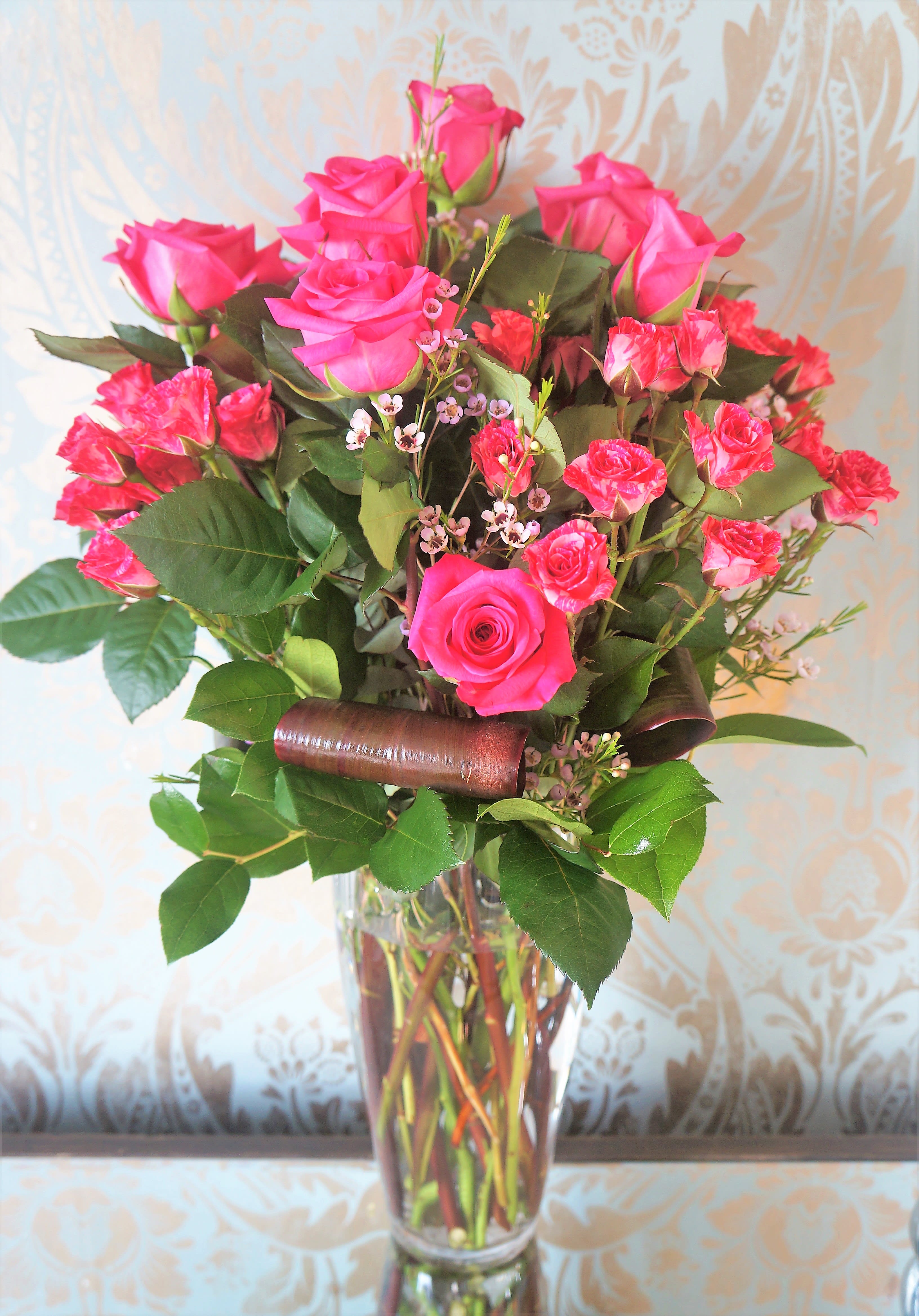 Tall bouquet of hot pink roses and spray roses in a clear glass vase