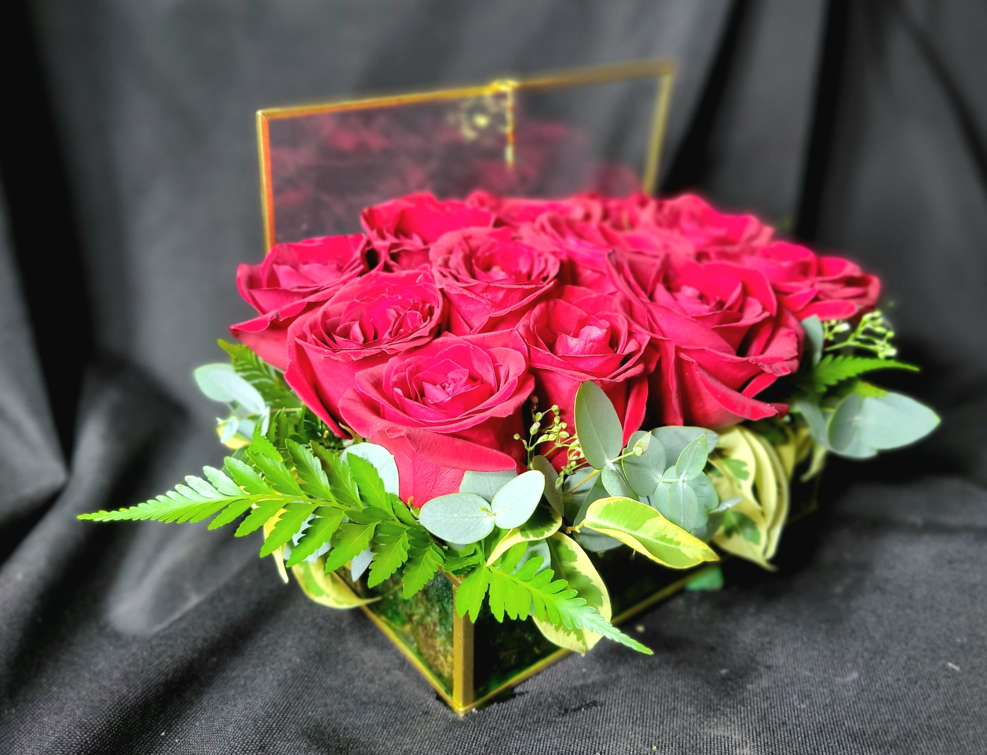 Box arrangement of red roses in a clear square container with the lid propped open