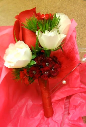 Red and white rose boutonniere with small red blooms, wrapped in red ribbon on pink tissue paper