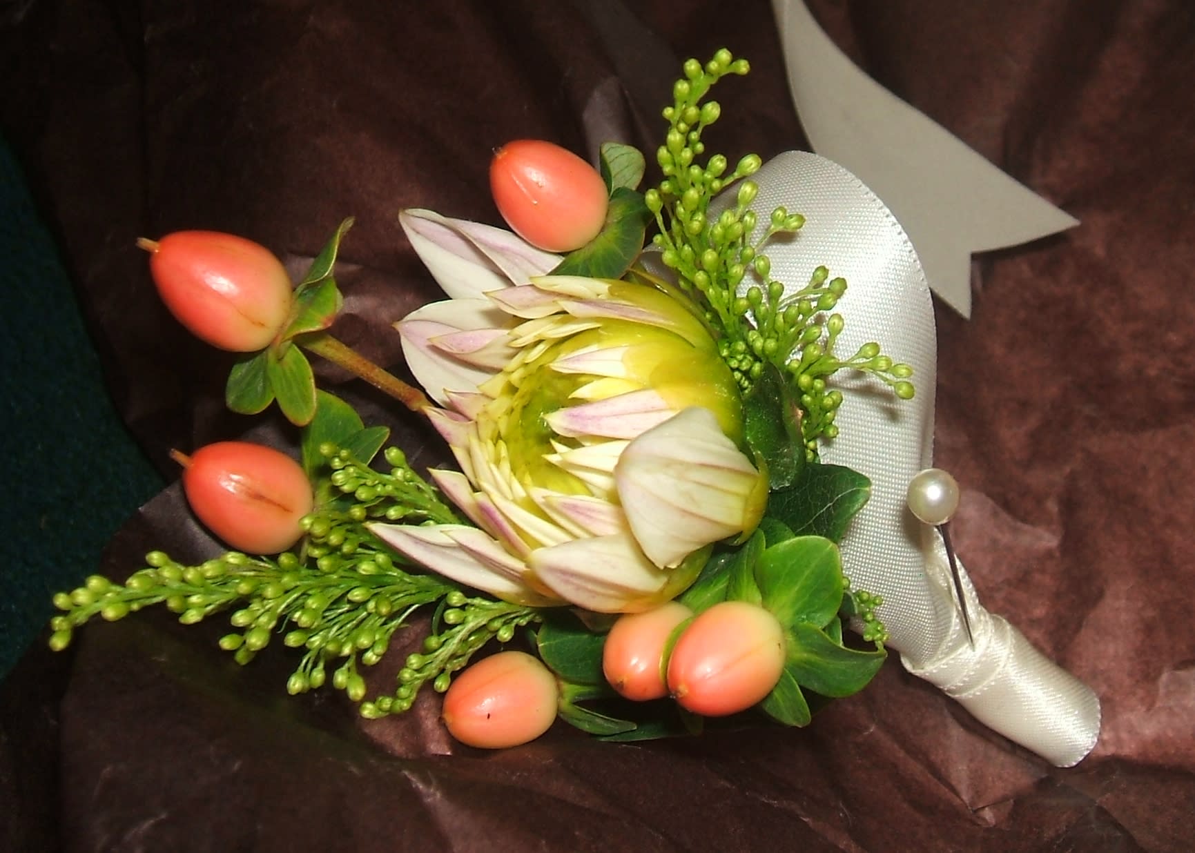 Cream and green protea boutonniere with pink berries wrapped in ivory ribbon and pearl pin