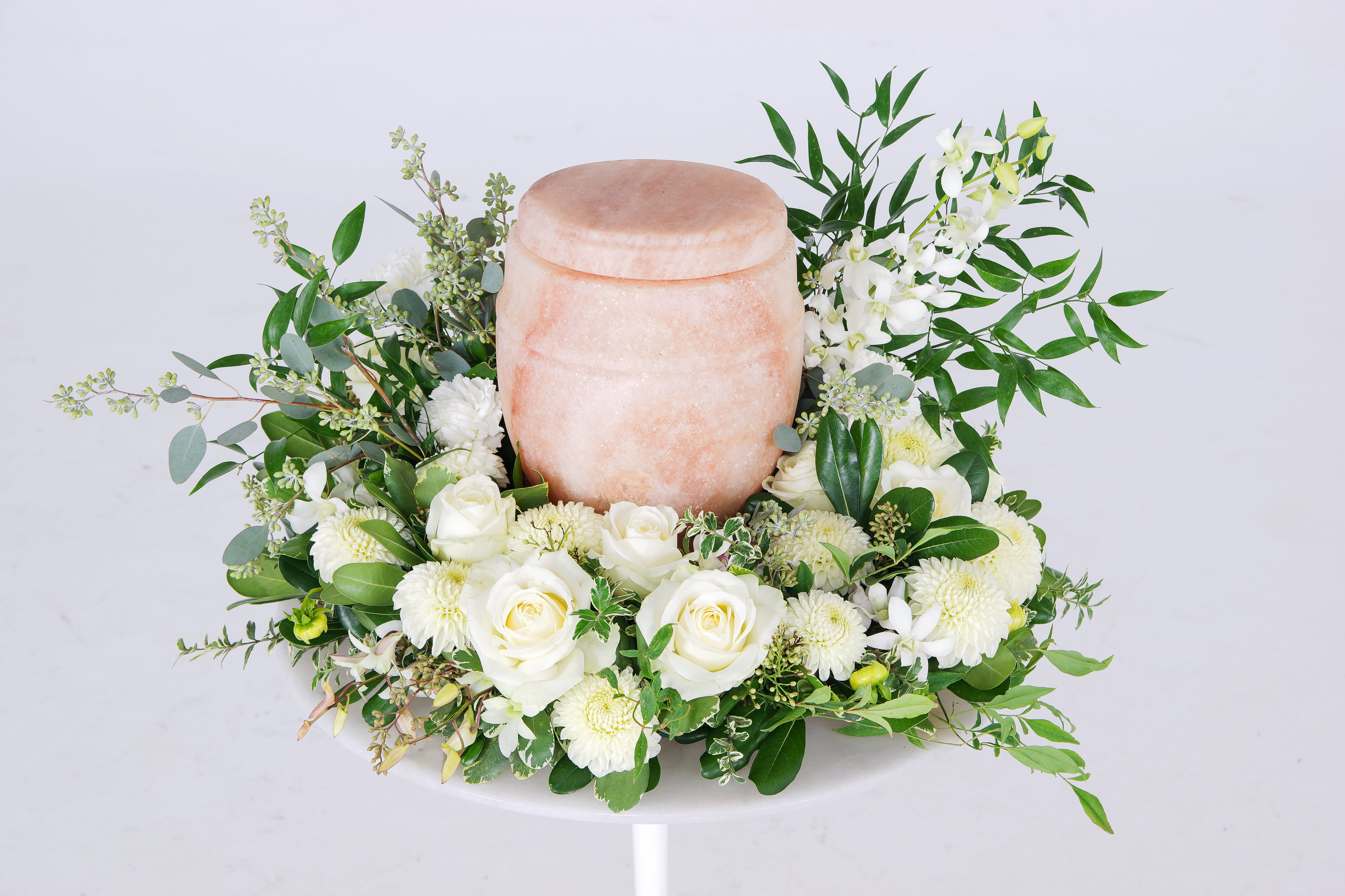 White roses and mums arranged around a pink urn-shaped vessel