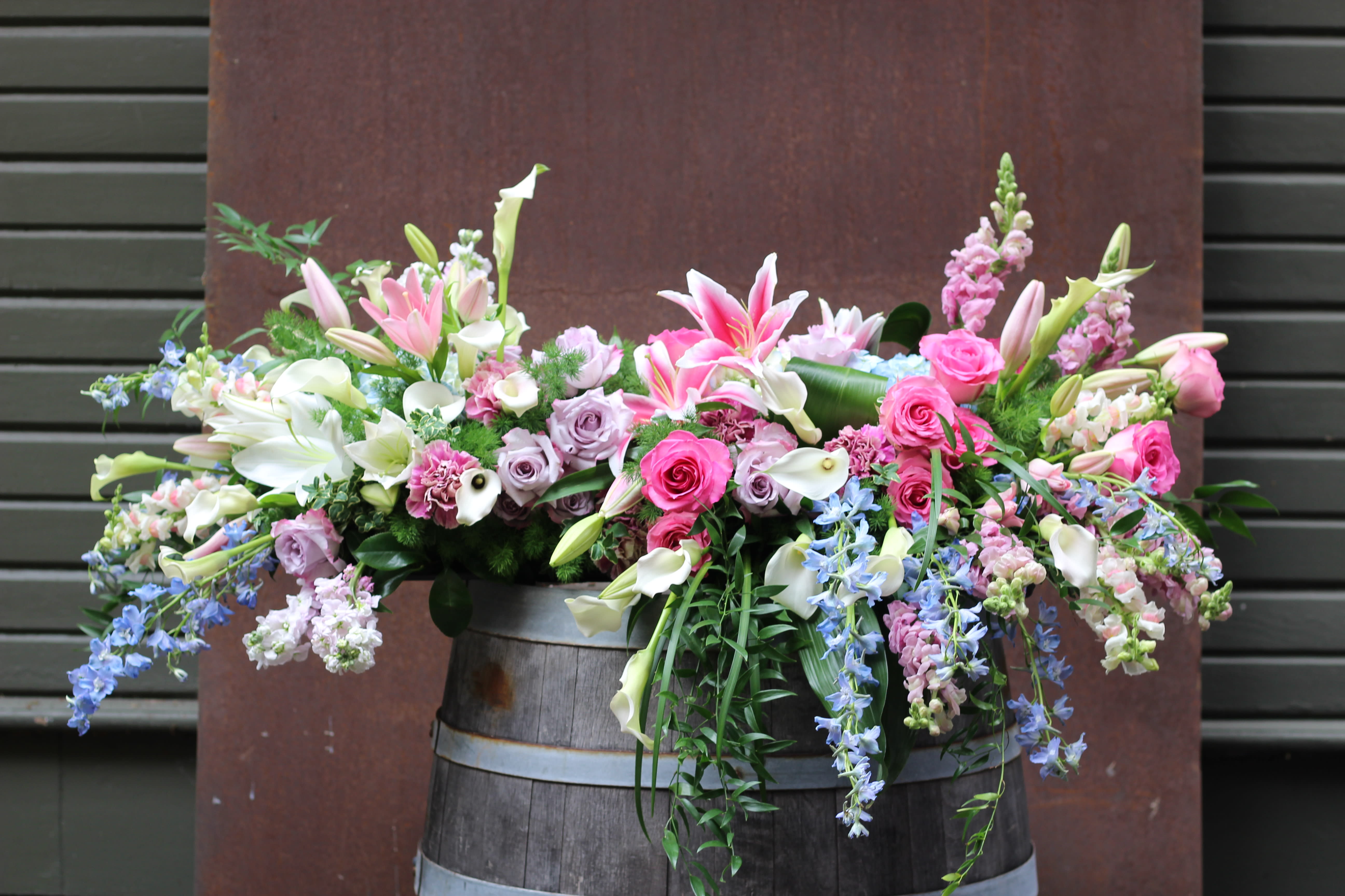Large mixed floral arrangement with lilies, roses, calla lilies, and snapdragons in a wooden barrel