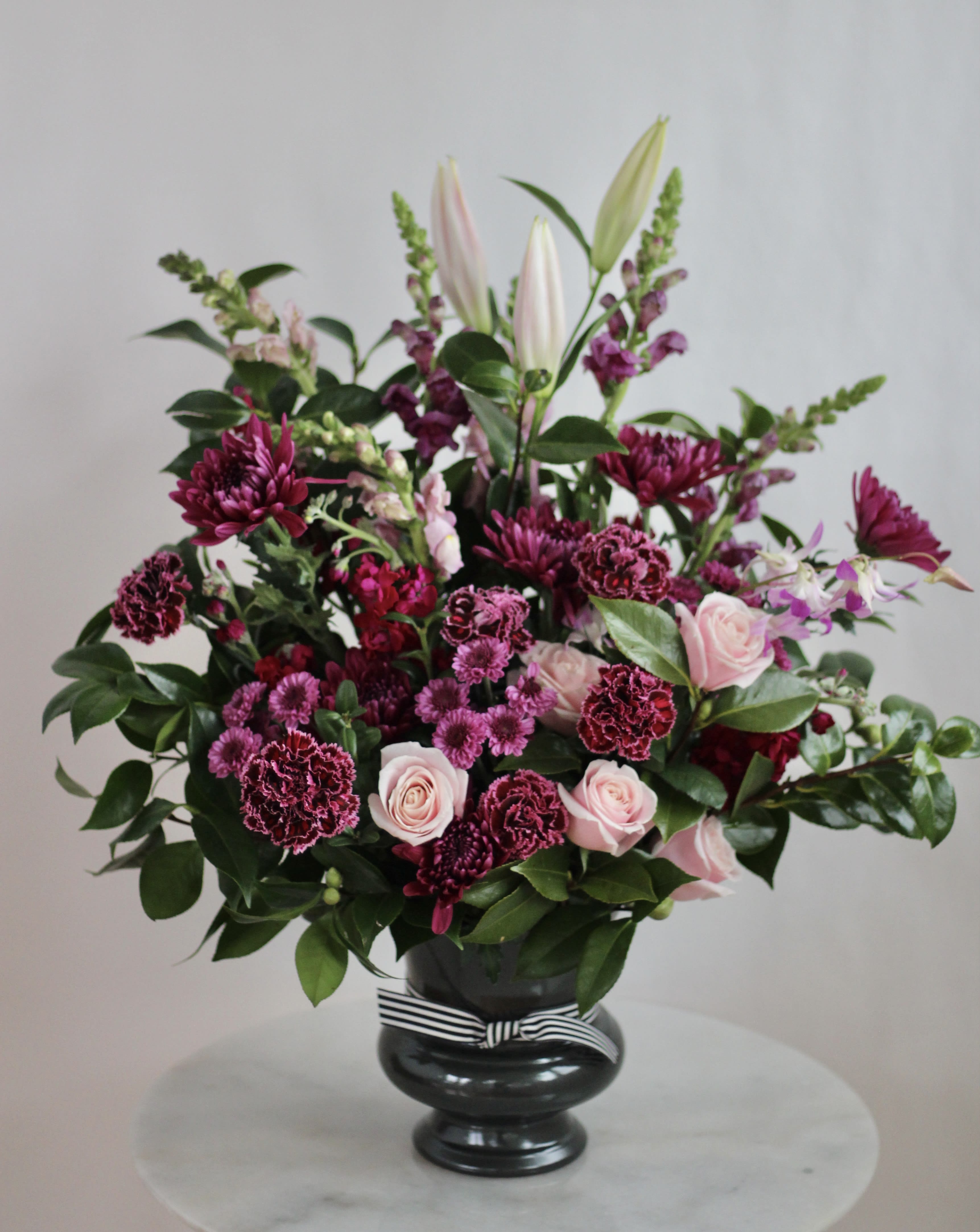 Pink and burgundy floral arrangement in a black vase