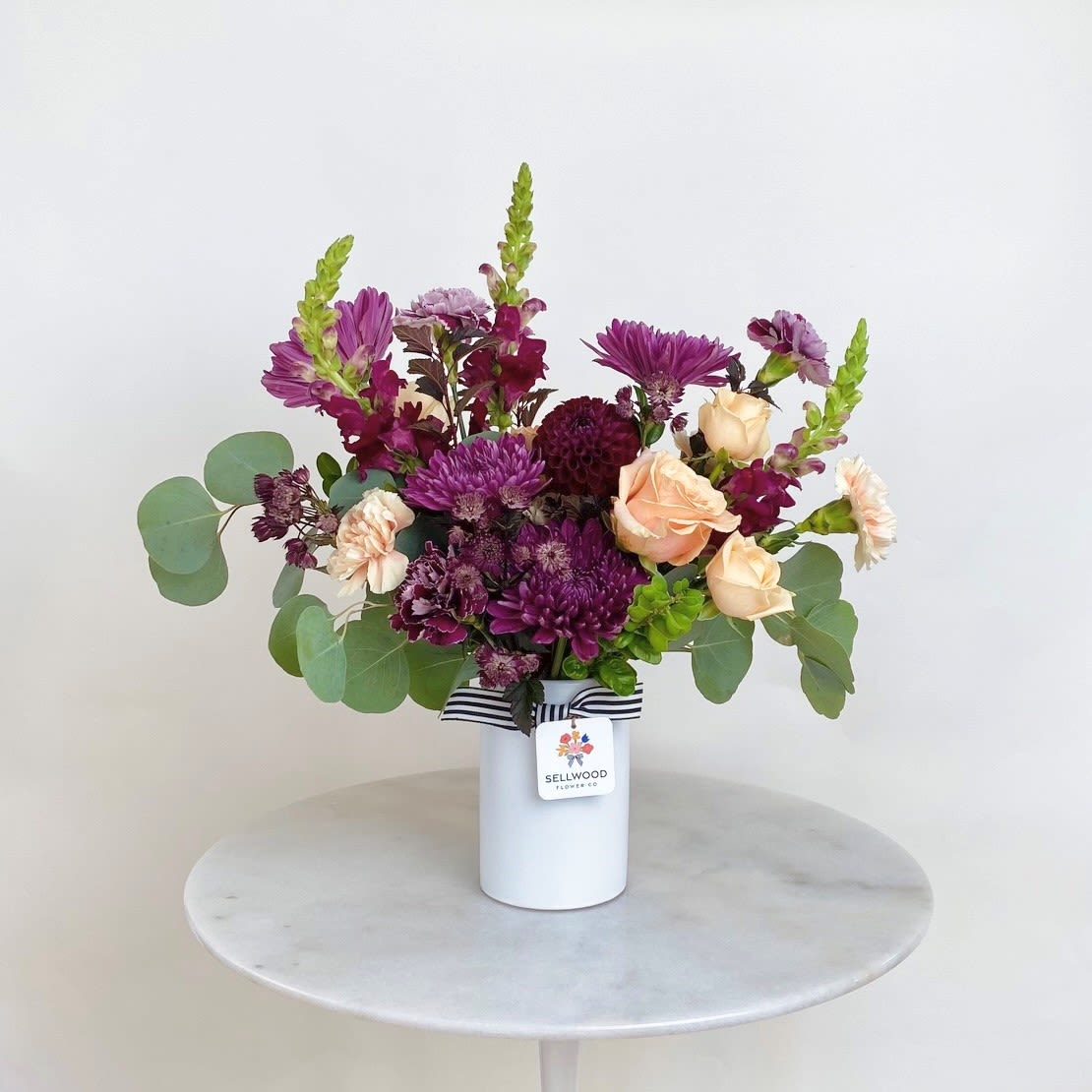 Purple and peach mixed bouquet in a white vase