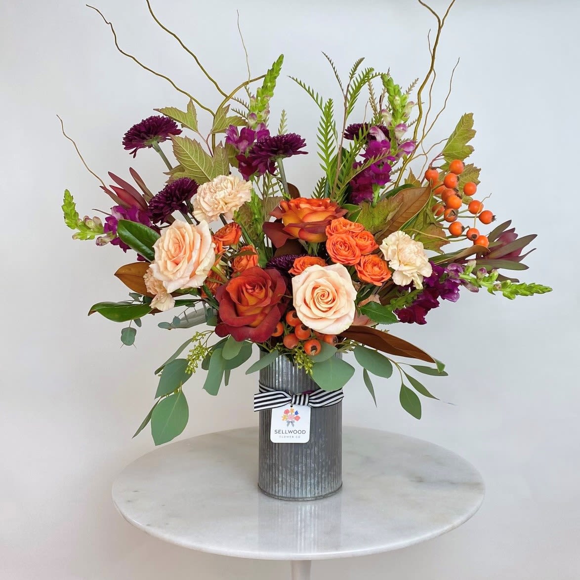 Mixed bouquet of roses, carnations, and purple blooms in a ribbed metal vase