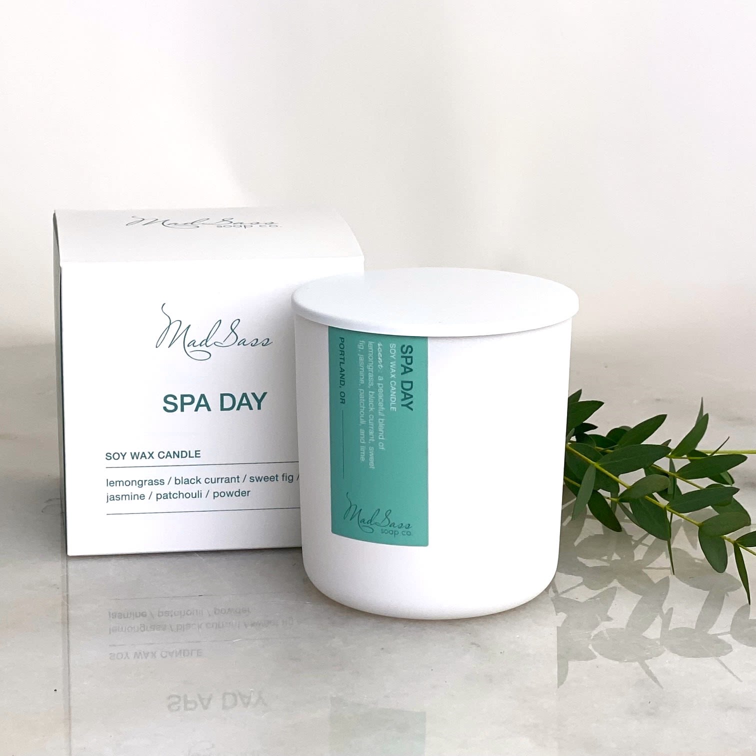 White soy wax candle in a box with green label and sprig of leaves