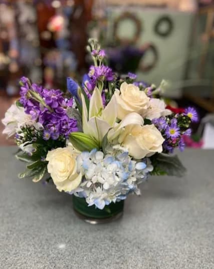 Bouquet of cream roses, lilies, and purple flowers in a glass vase