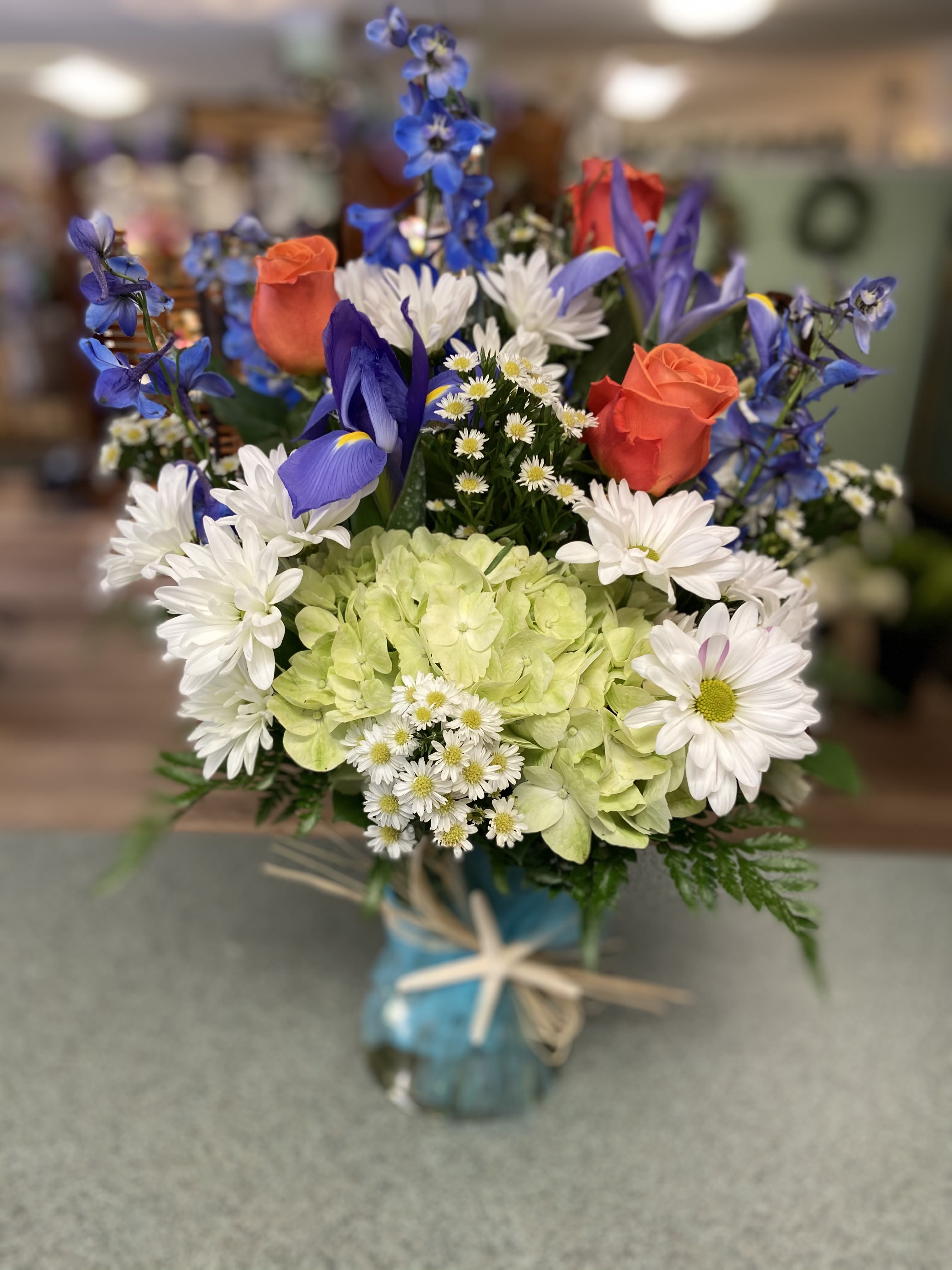Mixed bouquet with blue, white, and orange flowers in a glass vase