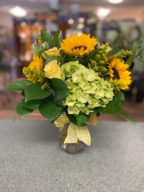Bouquet of sunflowers, pale green hydrangea, and yellow roses in a glass vase