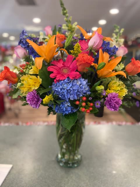 Colorful mixed bouquet in a glass vase with lilies, roses, hydrangeas, and daisies