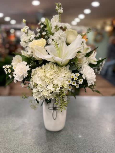 White floral arrangement in a tall vase with lilies and hydrangeas