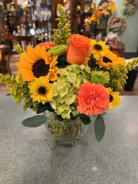 Bright bouquet with sunflowers, orange roses, and carnations in a glass vase