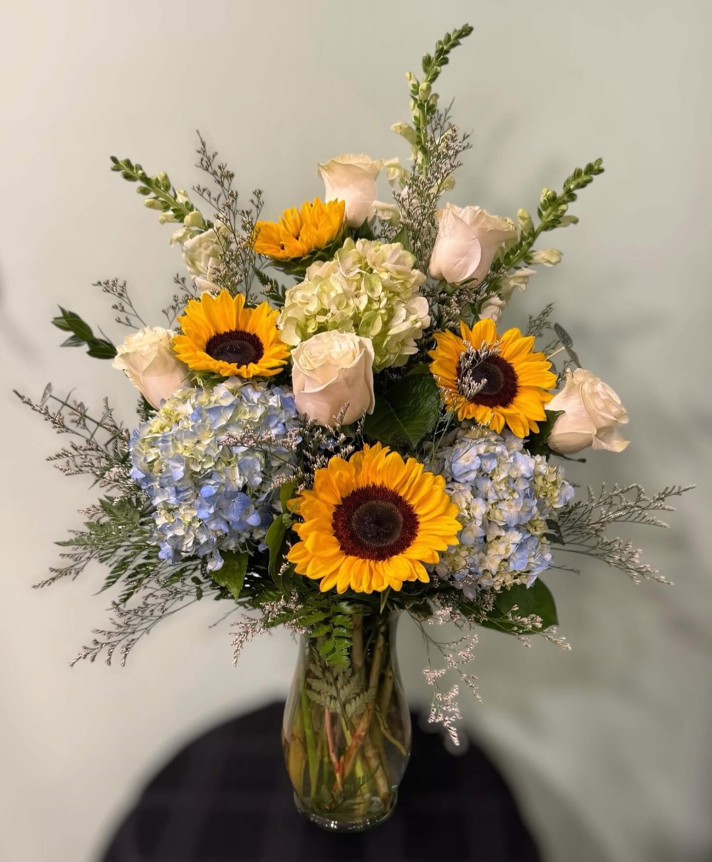 Bouquet of sunflowers, pale roses, and hydrangeas in a glass vase