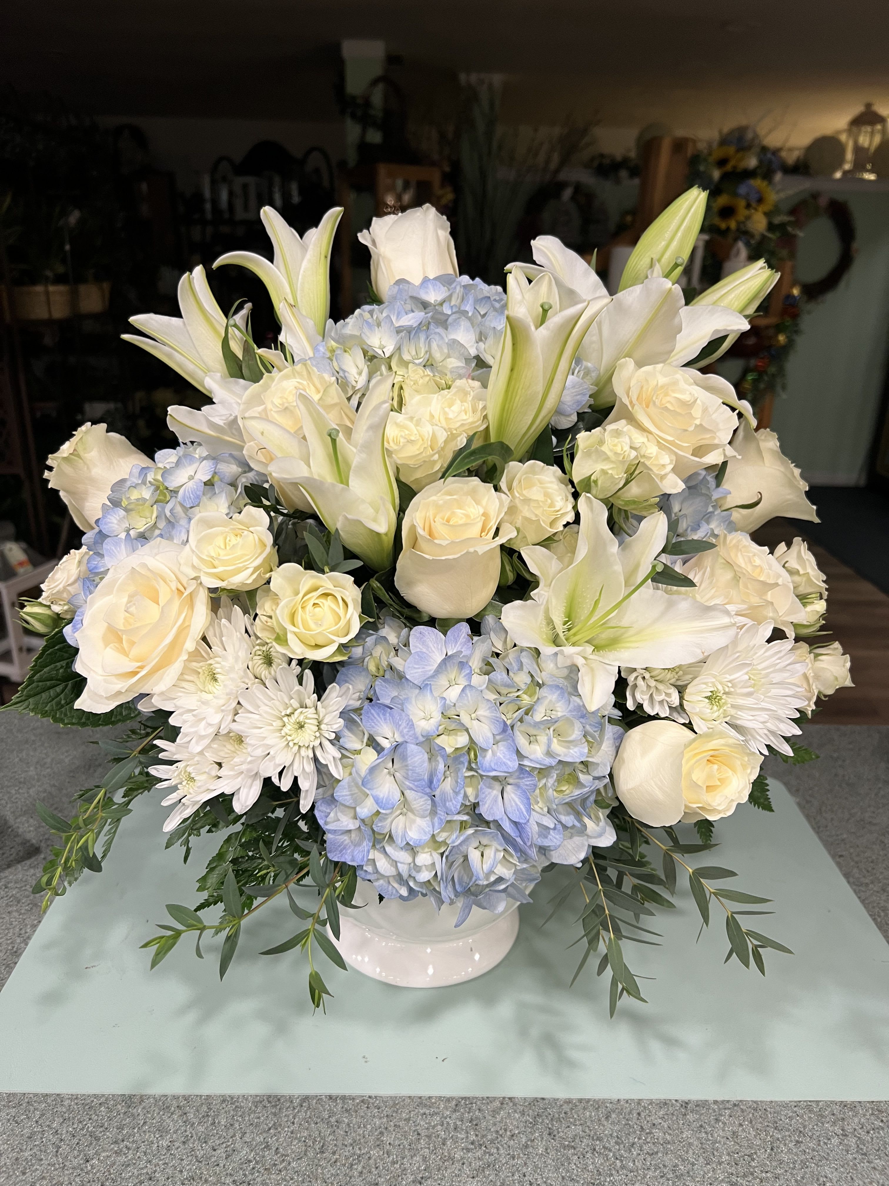 White lilies, roses, and blue hydrangeas arranged in a white vase