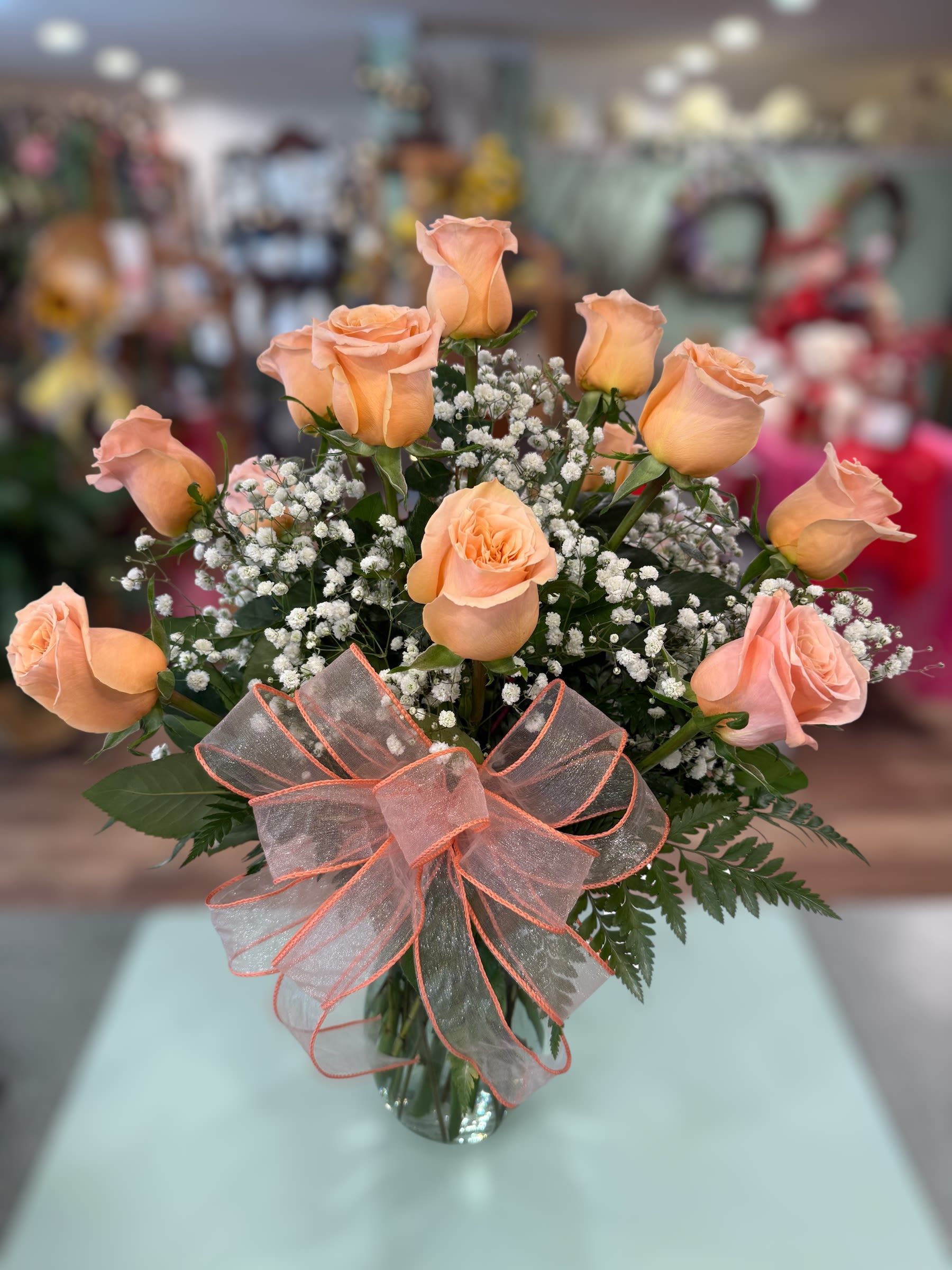 Peach roses in a glass vase with baby's breath and a sheer ribbon bow