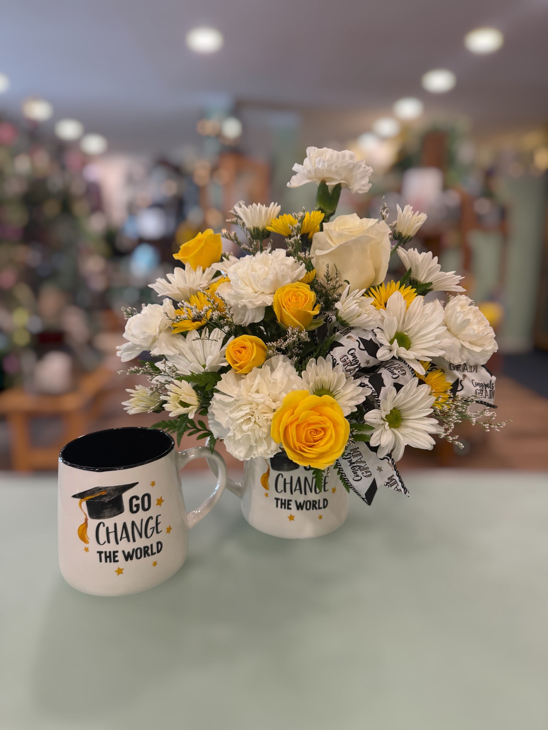 Go Change the World Mug (GCTW) - A bright white-and-yellow bouquet arranged in a "Go Change the World" keepsake ceramic mug. This design creates an instantly uplifting gift for graduation. The mug features yellow roses paired with white carnations and daisies for a fresh, celebratory feel-perfect for congratulating a new grad.