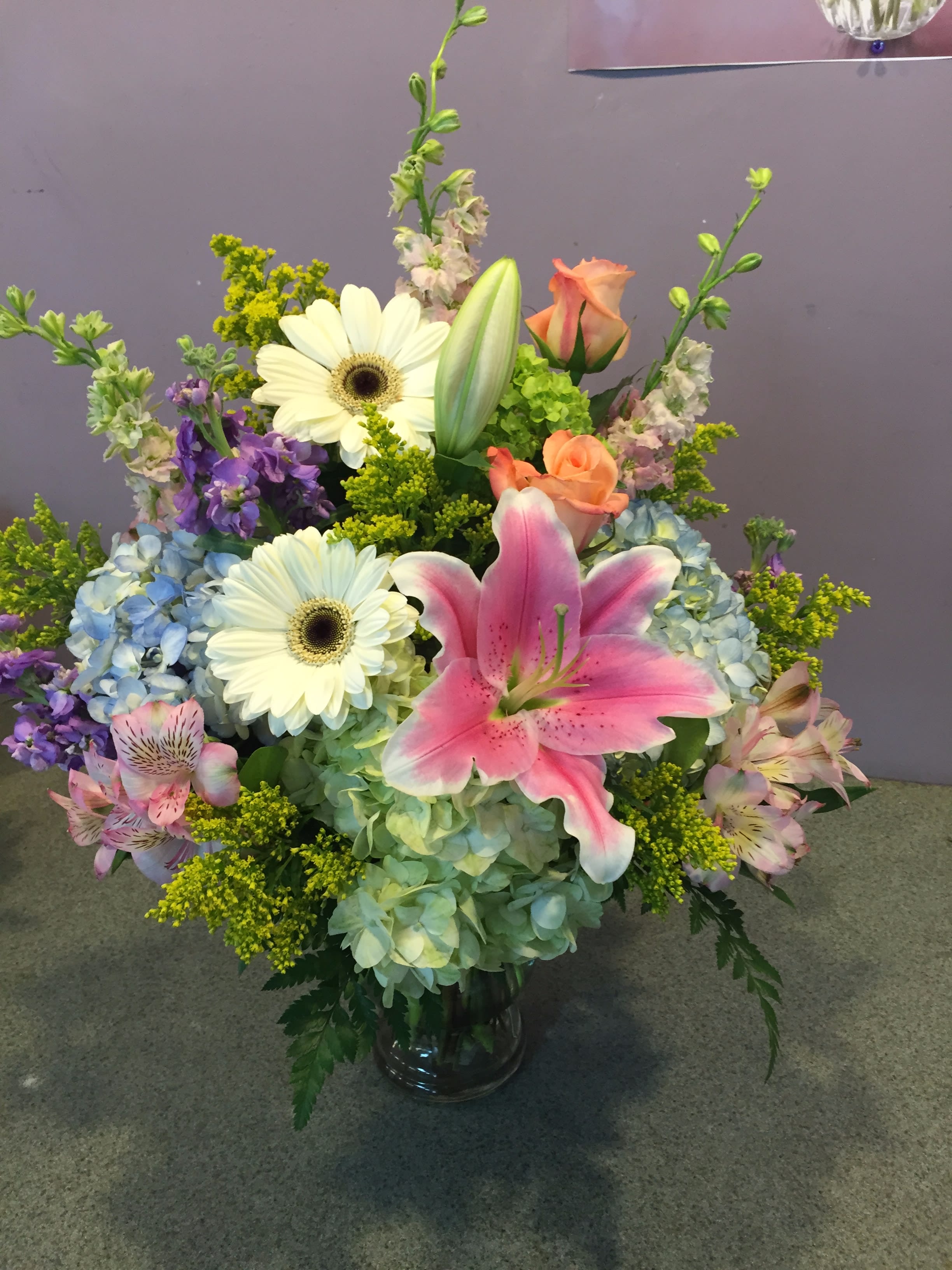 Mixed bouquet with pink lily, white daisies, and blue hydrangeas in a glass vase