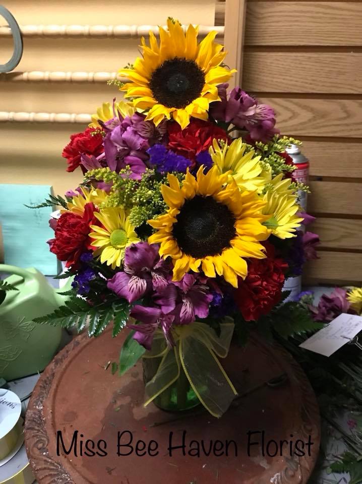 Bouquet with sunflowers, purple alstroemeria, and red carnations in a glass vase
