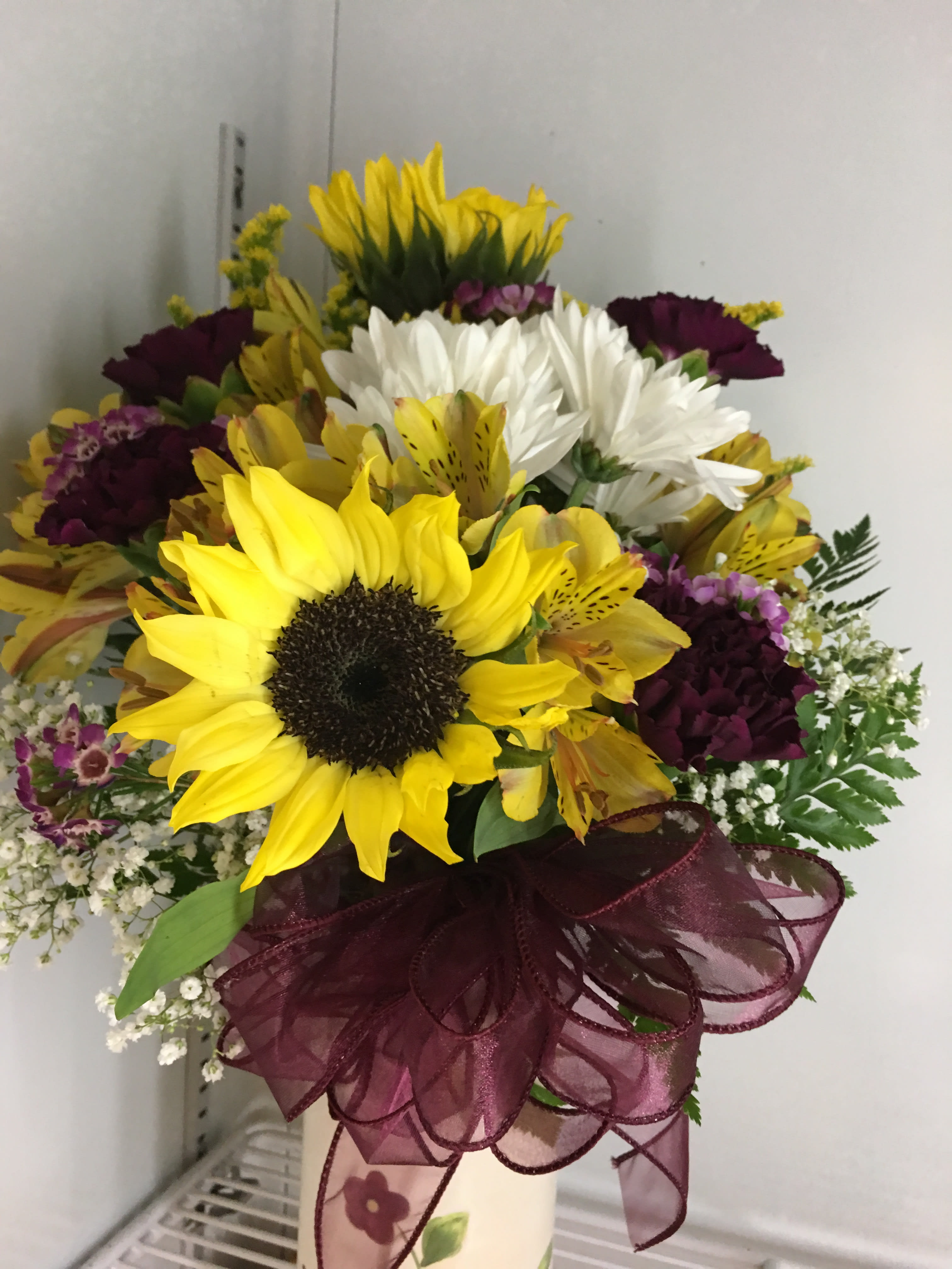 Bouquet of sunflowers, white daisies, and purple flowers with a burgundy ribbon