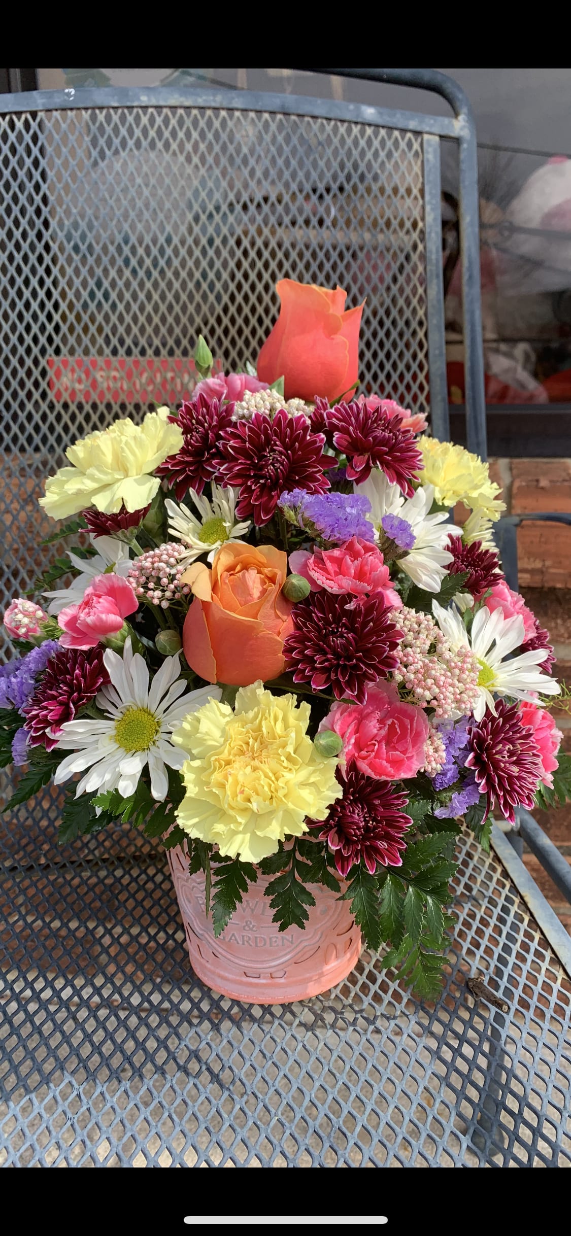 Mixed bouquet in a pink metal bucket with roses, daisies, and carnations