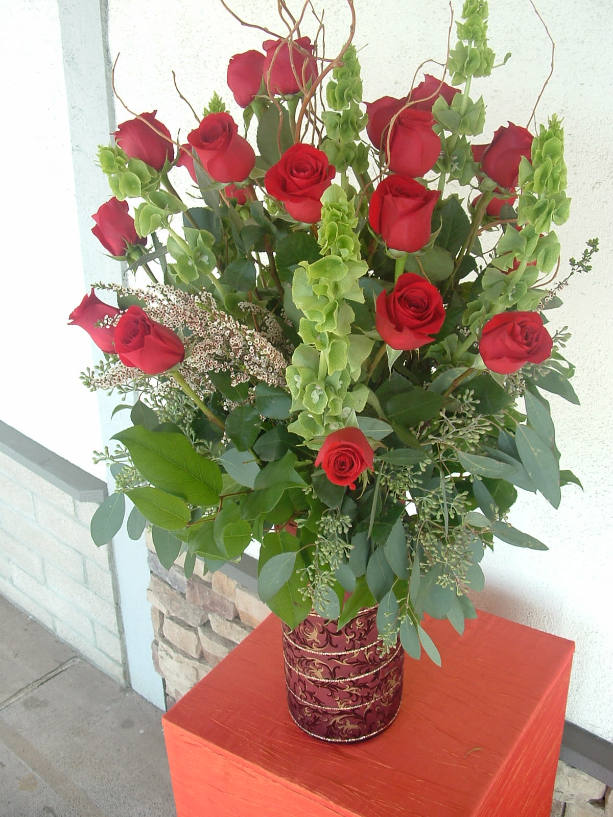 Tall bouquet of red roses with green filler in a decorative vase