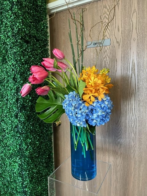 Pink tulips with blue and yellow flowers in a tall blue vase