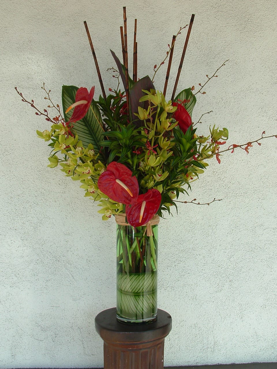 Tropical flower arrangement in a tall glass vase with red anthuriums