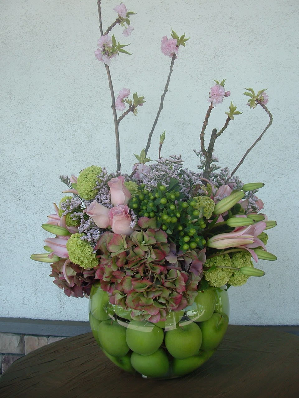 Pink flowers and green apples arranged in a glass bowl