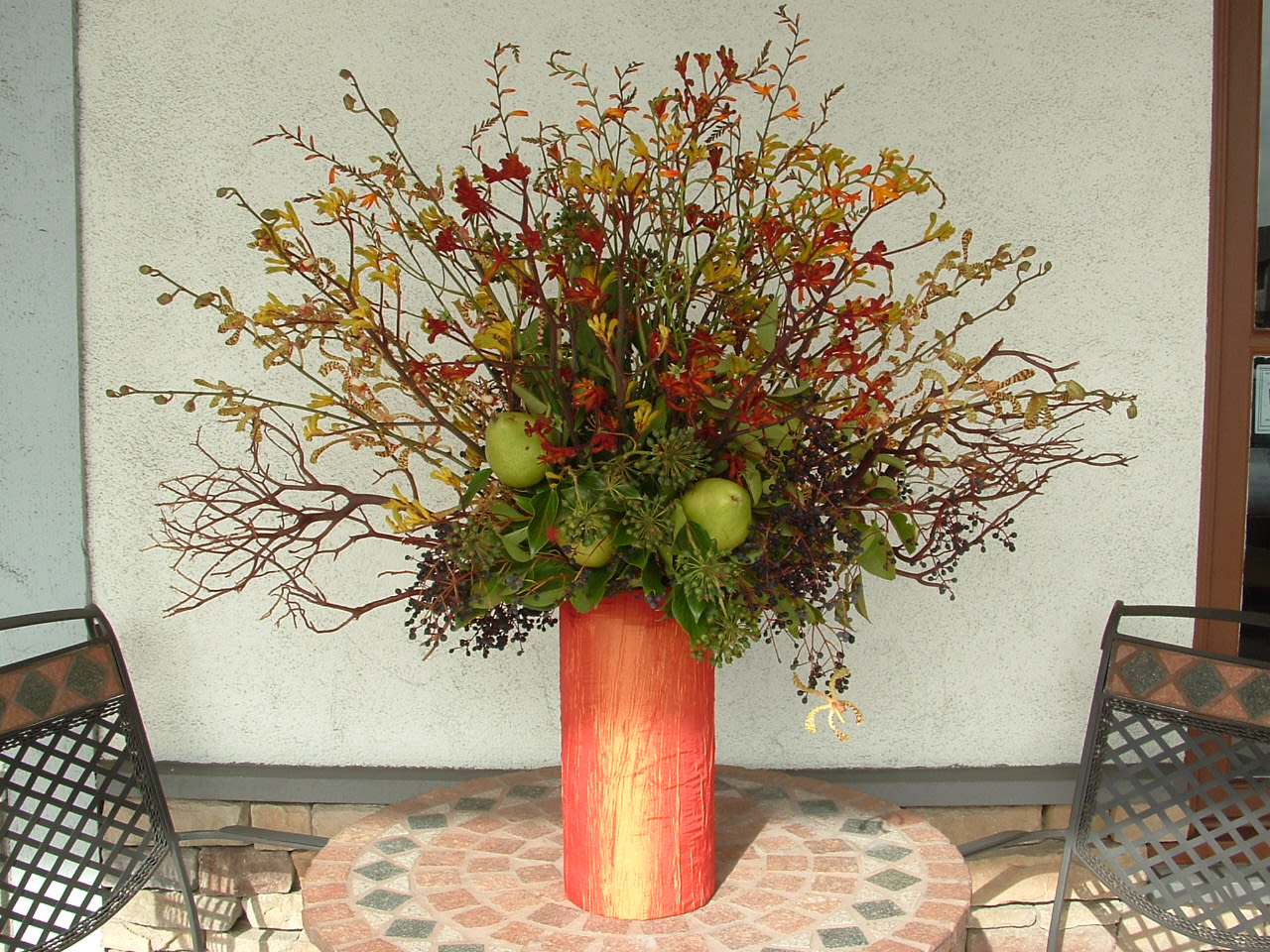 Tall autumn floral arrangement in a red vase with apples