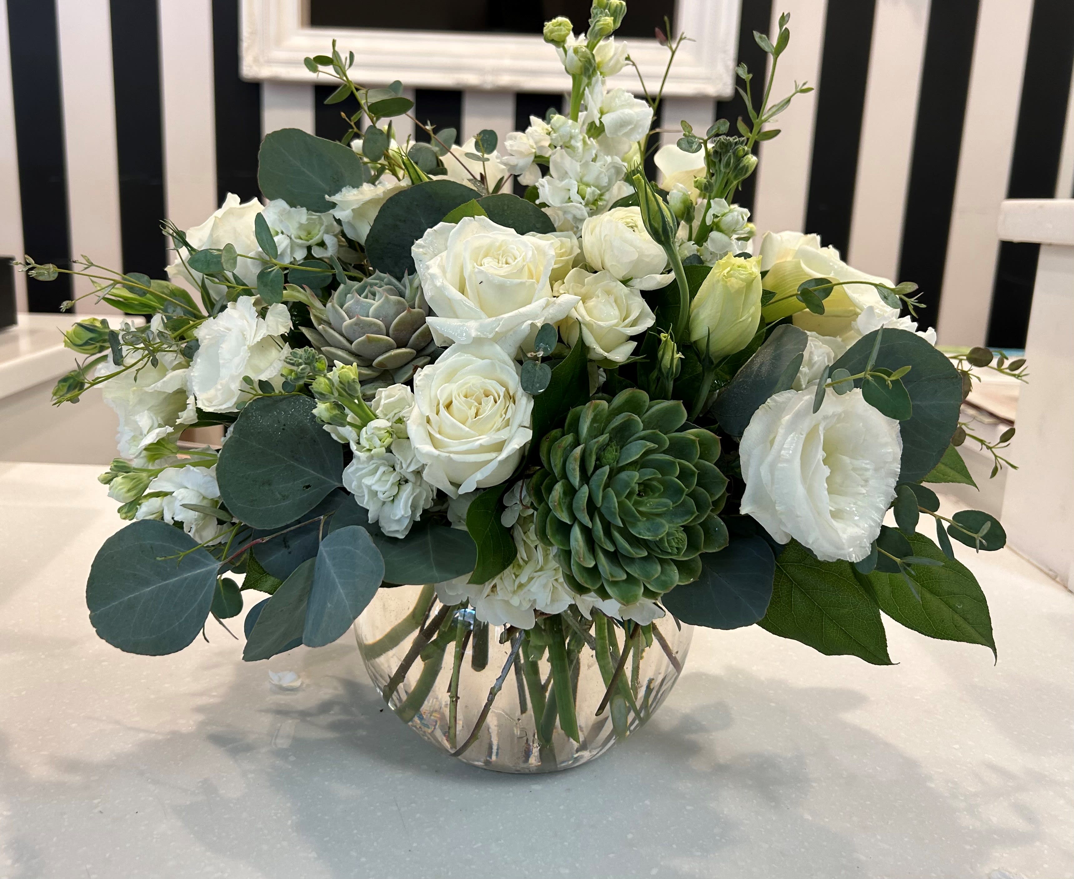 White roses and greenery arranged in a clear glass vase with succulents.