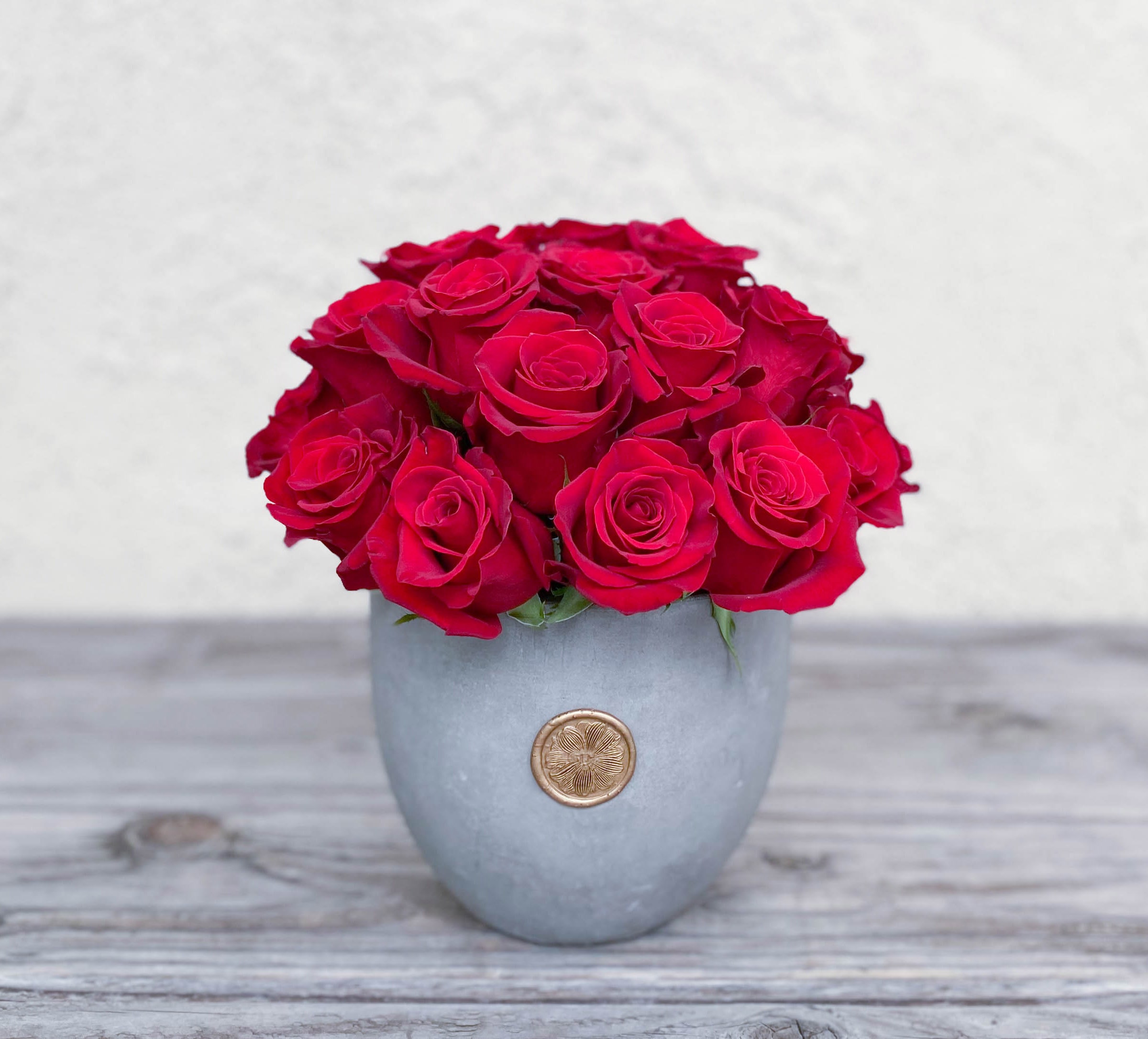 Red roses arranged in a gray vase with a gold emblem