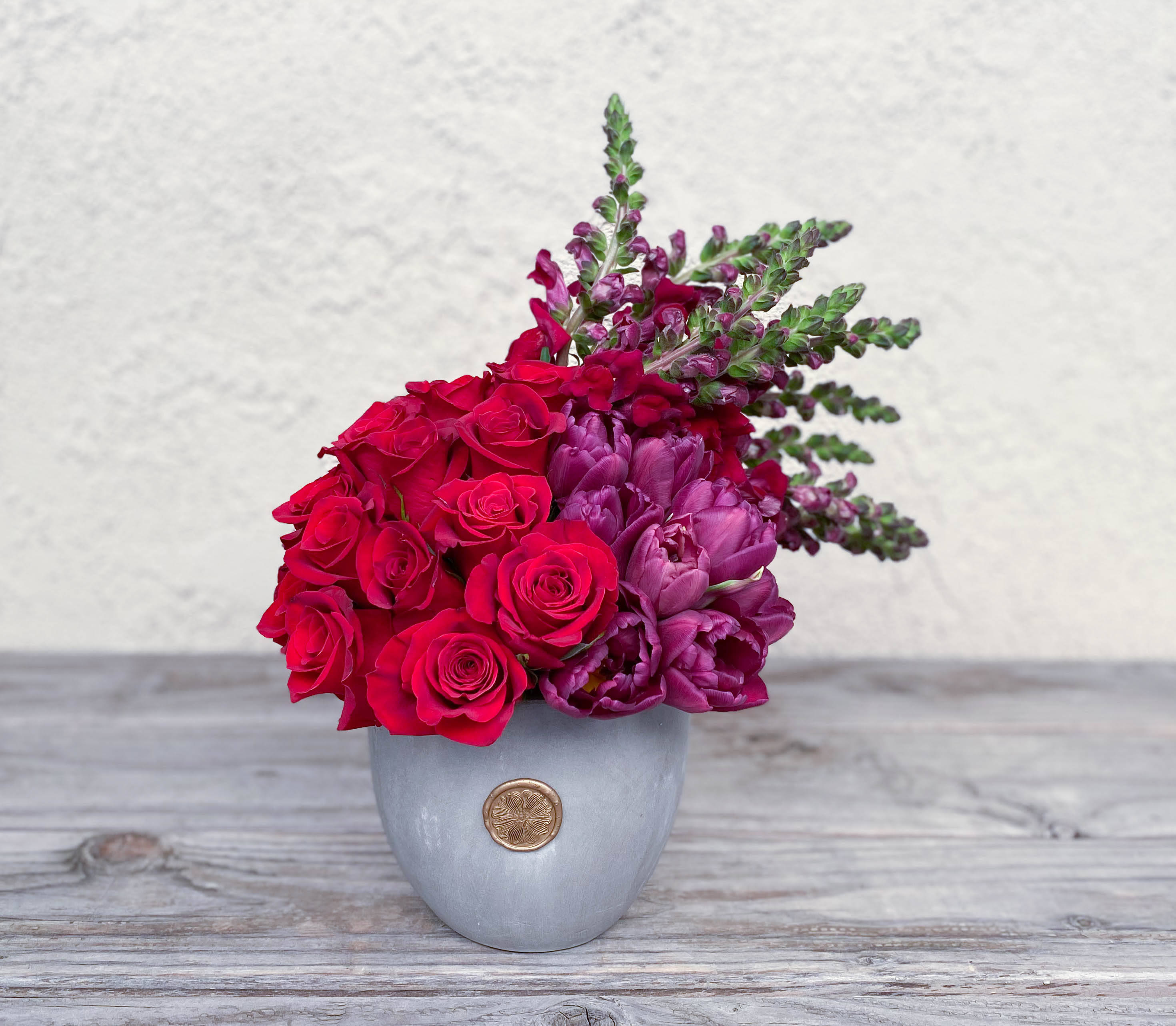 Red roses and purple flowers arranged in a gray vase