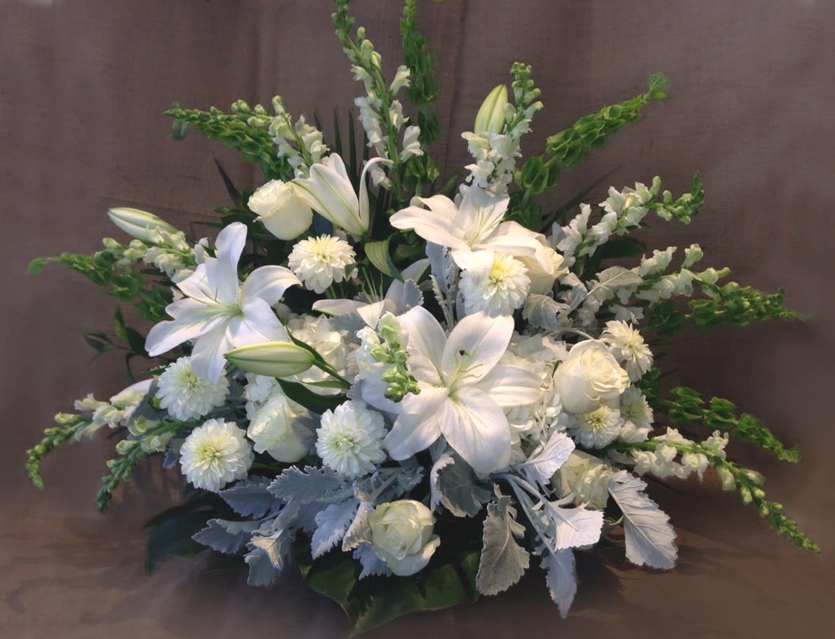 Large all-white floral arrangement with lilies, roses, and mums with green accents in a fan shape