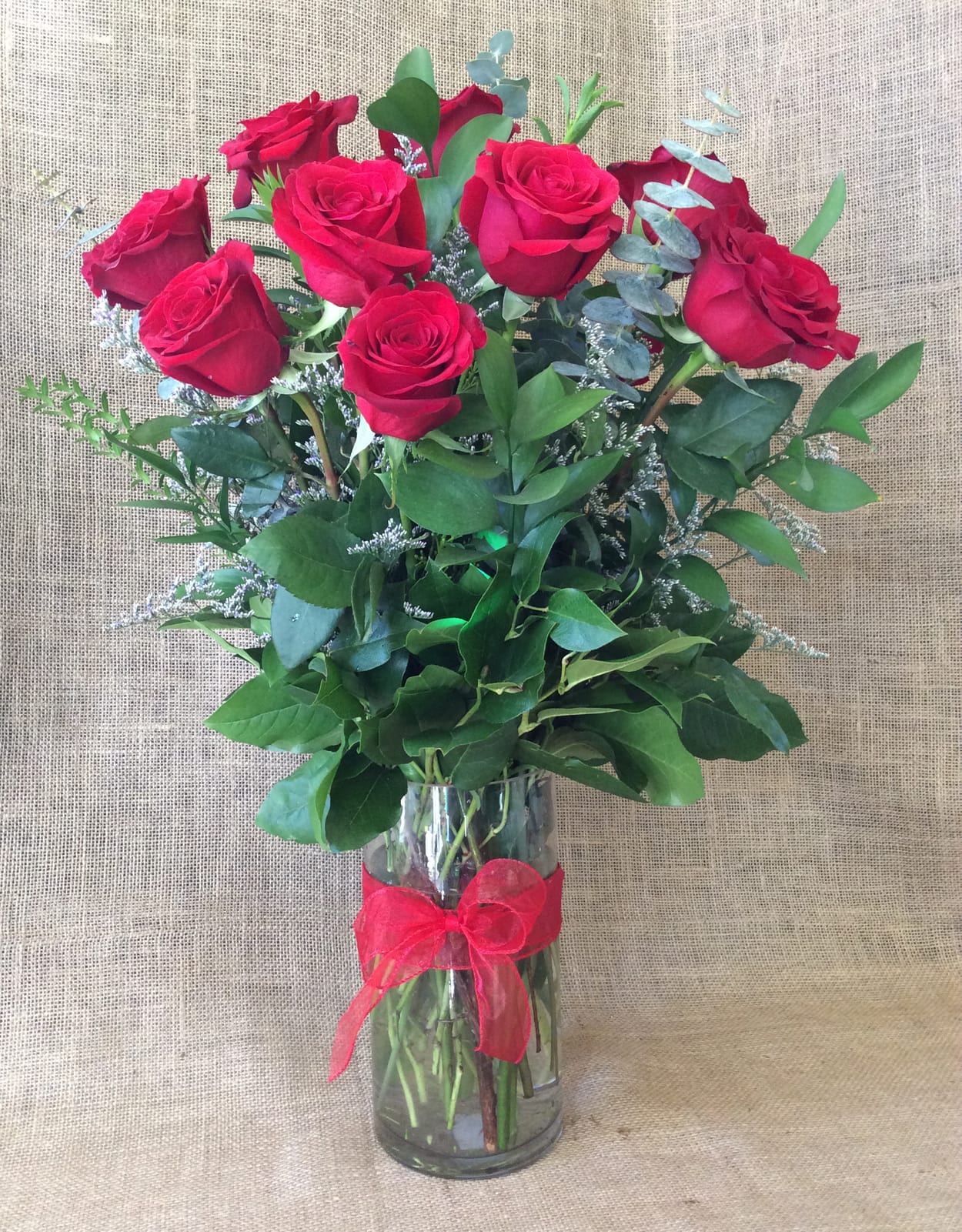 Tall arrangement of red roses in a clear glass vase with a red bow