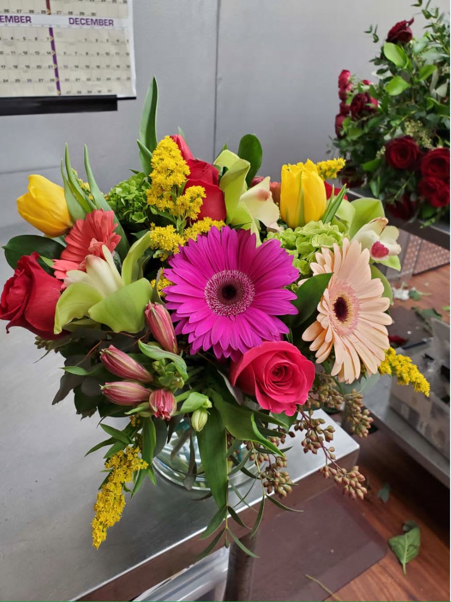 Bright mixed bouquet of gerbera daisies, roses, and tulips in a clear glass vase