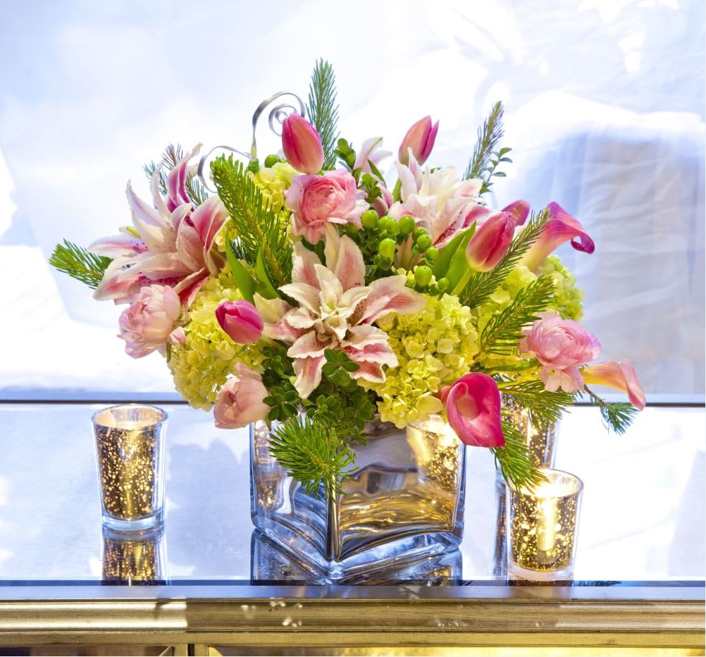 Low arrangement of pink lilies, calla lilies, tulips, and yellow hydrangeas in a glass cube with votive candles