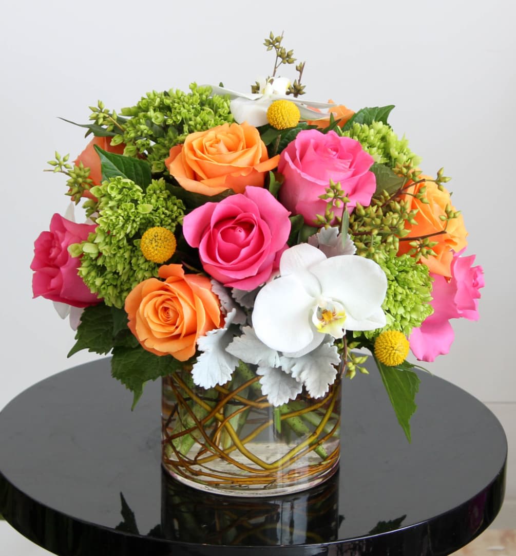 Mixed bouquet of pink and orange roses with white orchids in a clear glass cylinder vase