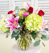 Bouquet of pink lilies, red roses, and green hydrangeas in a glass vase